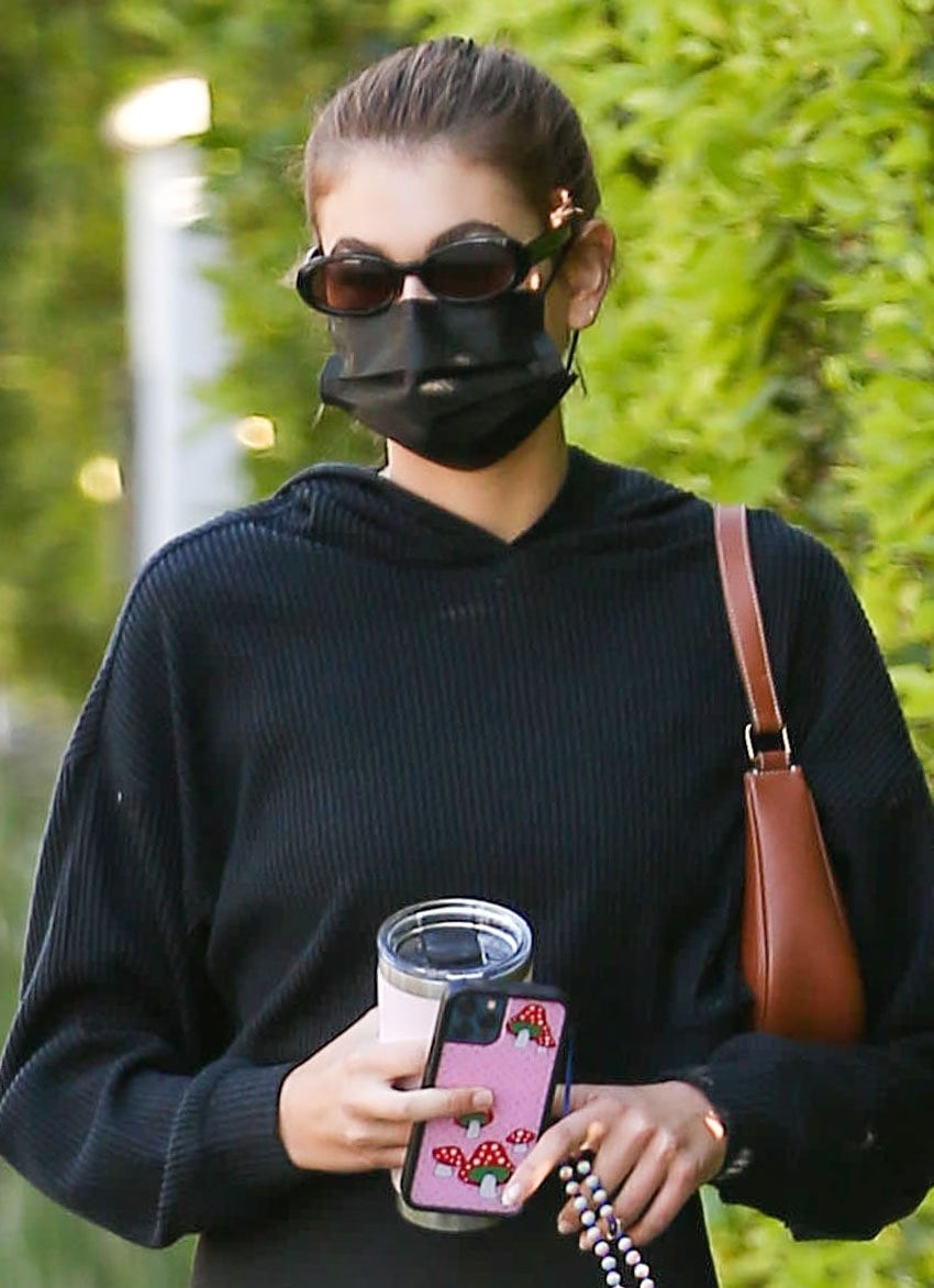 Kaia Gerber pulls tresses into a high ponytail and covers her face with oval-framed sunglasses and a black face mask