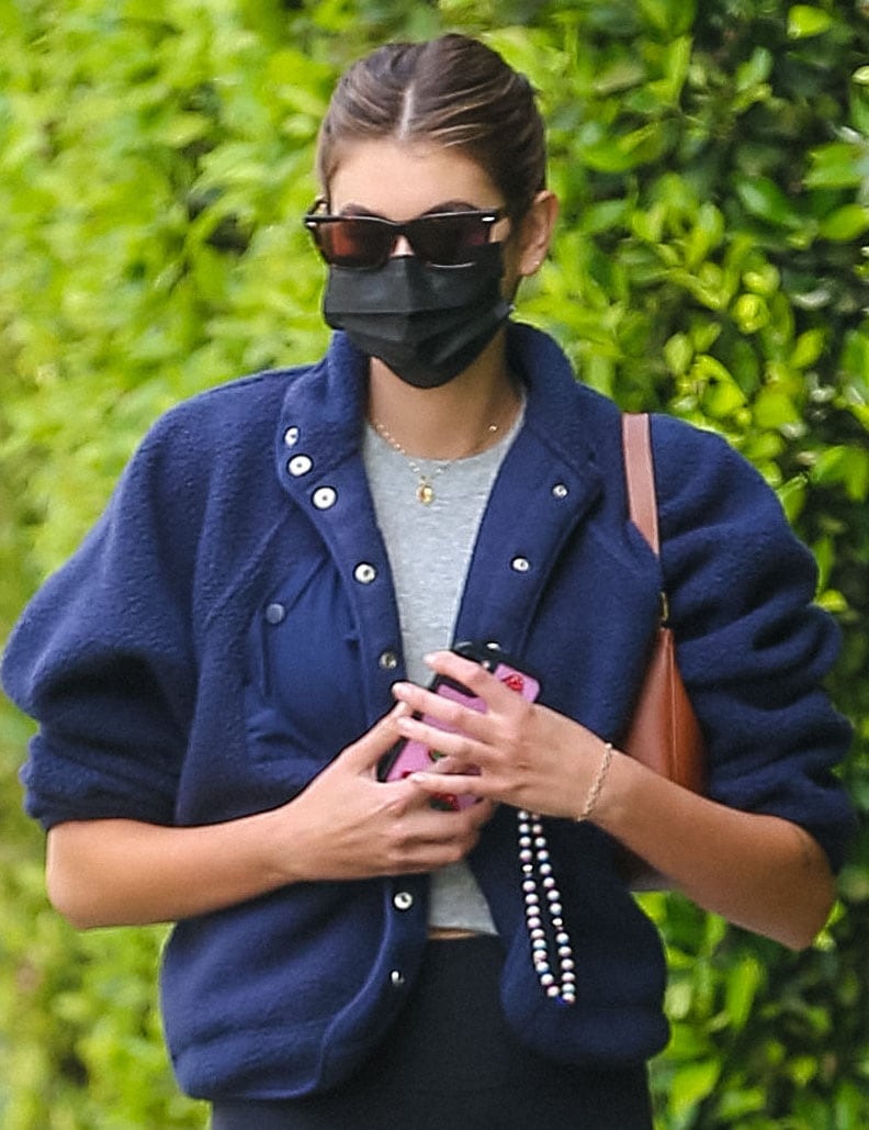 Kaia Gerber wears a ponytail and styles with tortoiseshell sunglasses, a Celine bag, and a black face mask