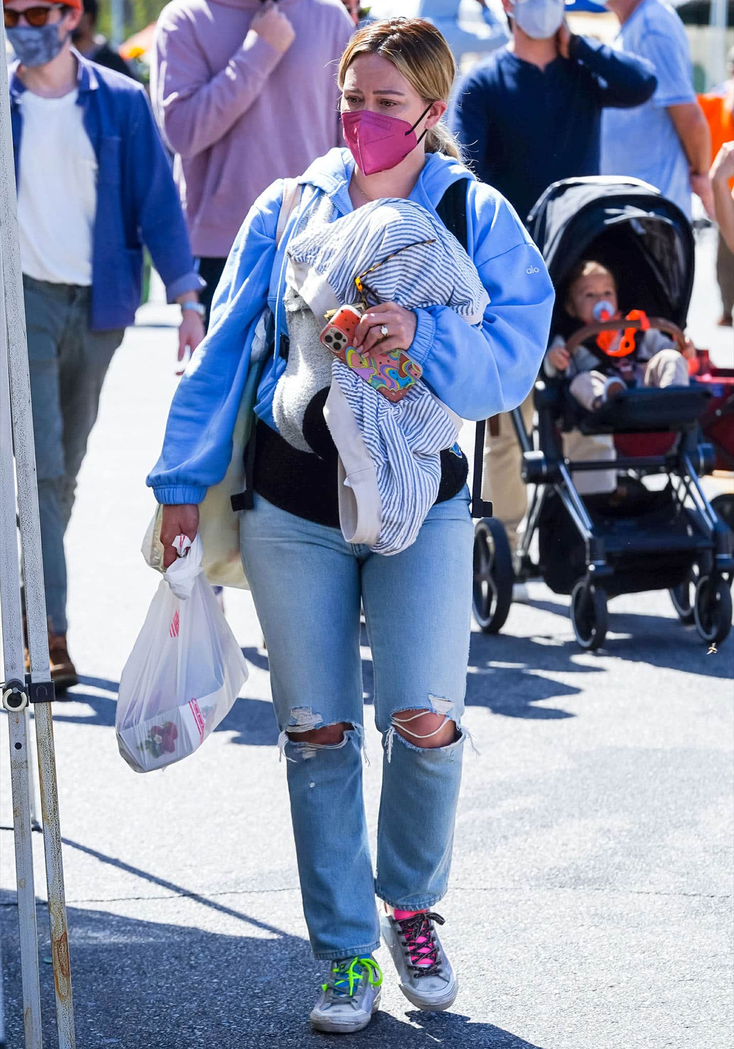 Hilary Duff carries her newborn daughter Mae while clad in an Alo Yoga hoodie and Agolde ripped jeans