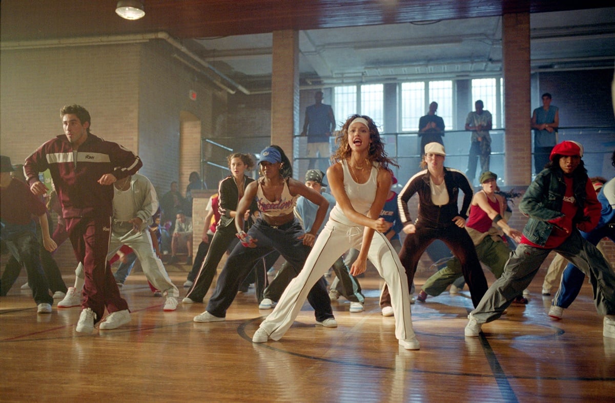 Jessica Alba, as Honey Daniels, leads a high-energy rehearsal scene with Jull Weber (Joey), wearing a white tank top, matching pants, and crisp white sneakers that grounded her choreography in early-2000s street style