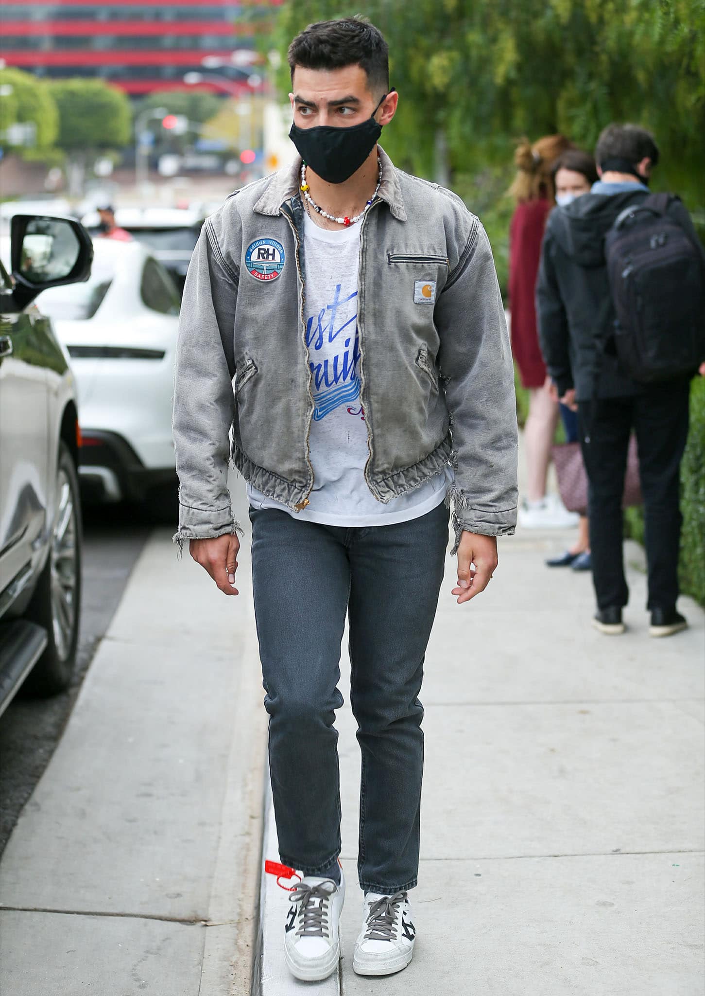 Joe Jonas keeps a casual look with a white graphic tee, a gray denim jacket, denim jeans, and Off-White shoes