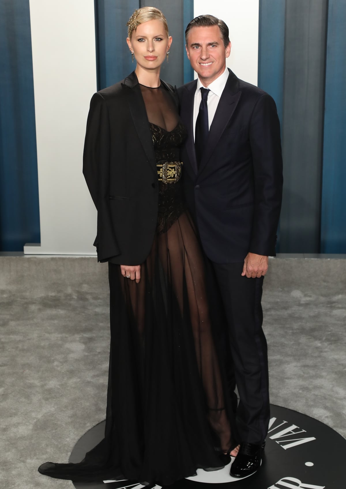 Karolina Kurkova exudes elegance in a sheer black gown paired with a structured blazer, while posing with her husband Archie Drury at the Vanity Fair Oscar Party