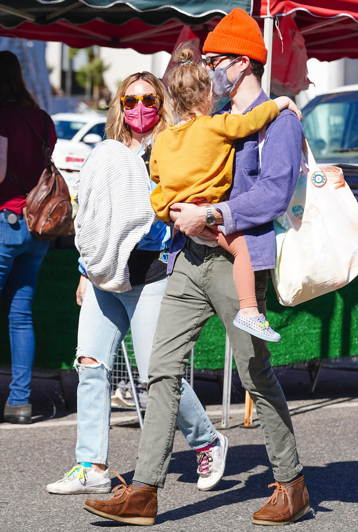 Matthew Koma looks cool in a purple shirt with green jeans and brown shoes as he carries their 2-year-old daughter Banks