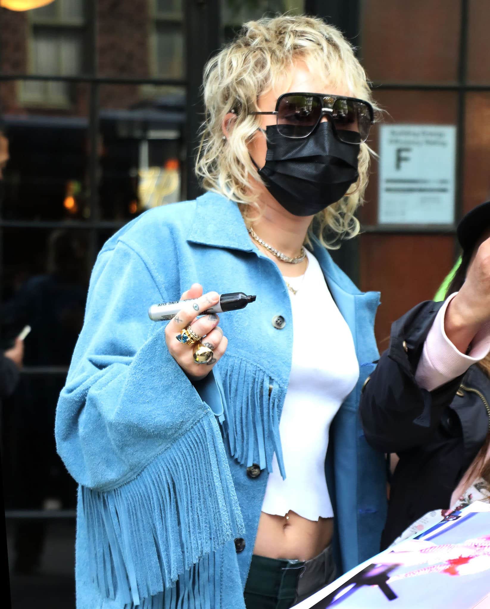 Miley Cyrus wears shaggy blonde hairstyle and hides her face behind rectangular sunglasses and a black face mask