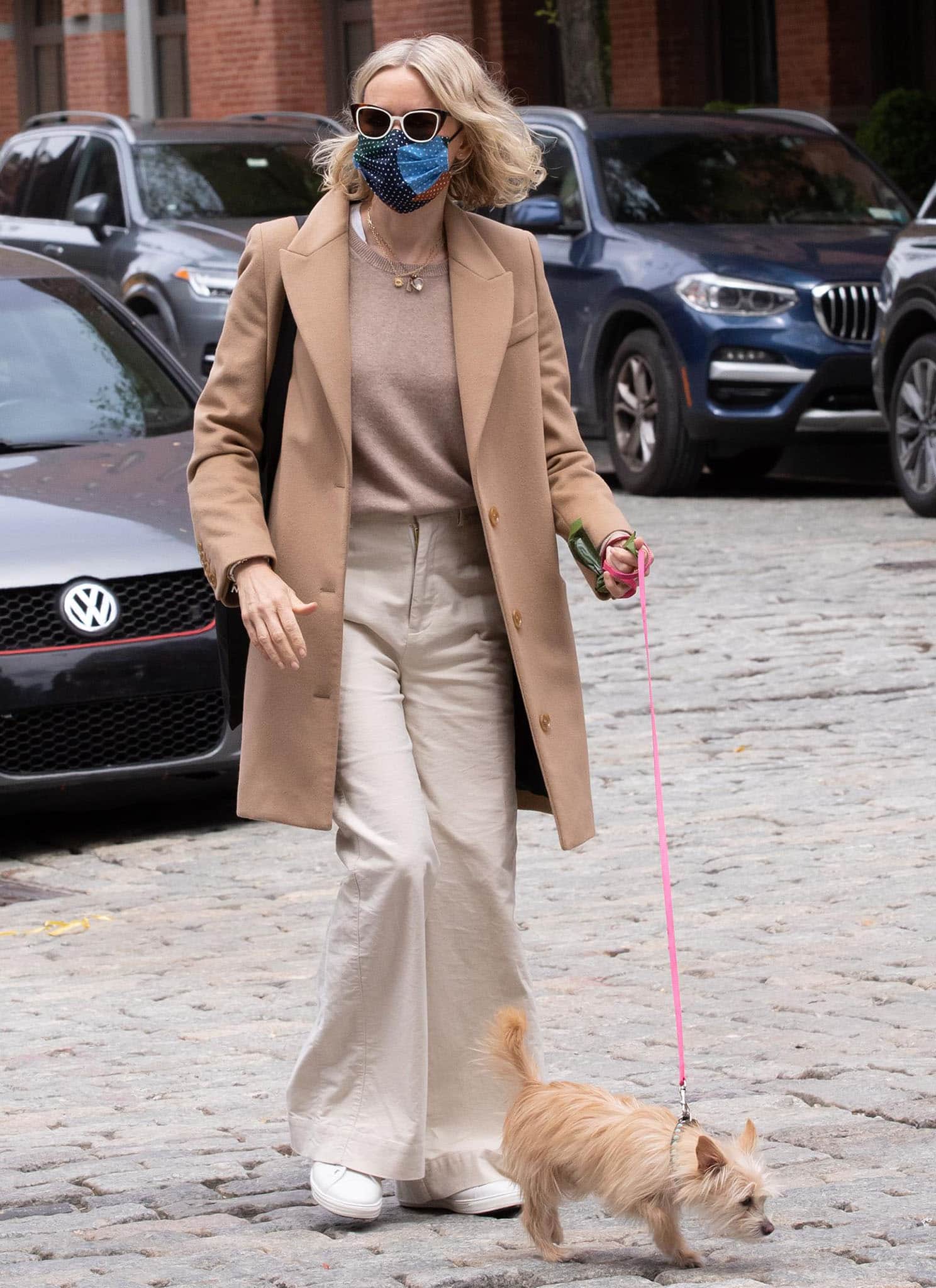 Naomi Watts opts for a neutral-colored outfit with a camel coat, a beige sweater, and cream pants
