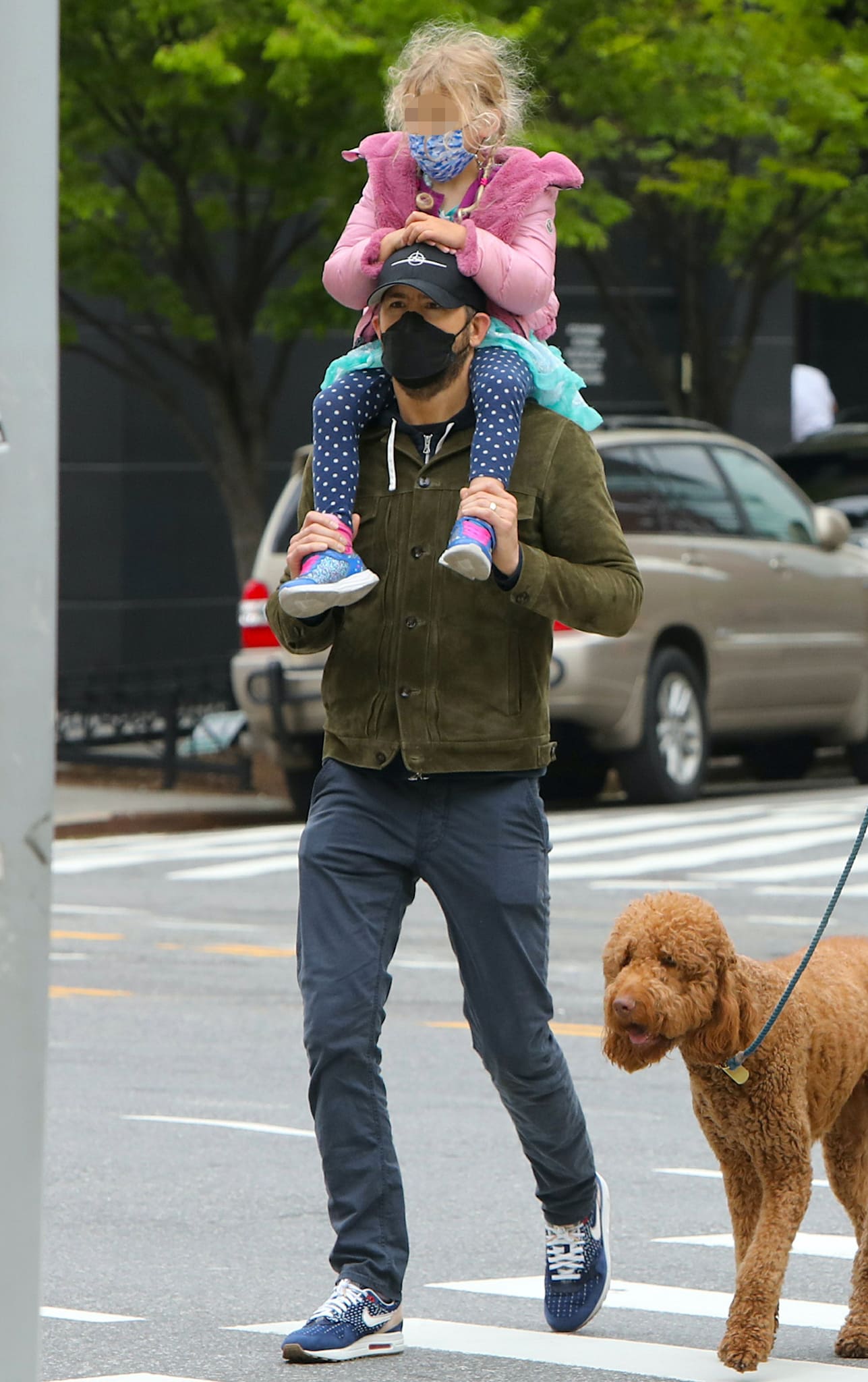 Ryan Reynolds carries his daughter on his shoulders in green jacket, navy pants, and Nike shoes