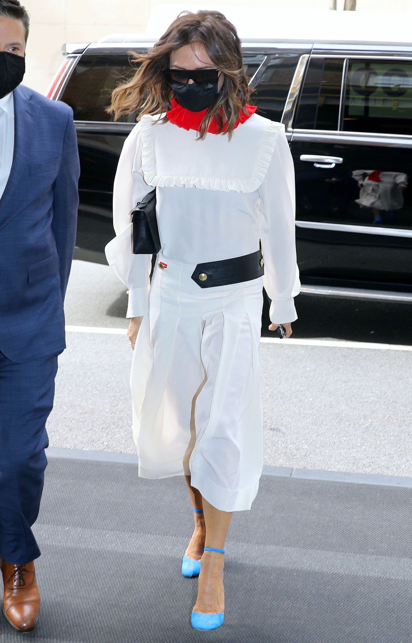 Victoria Beckham steps out of her hotel in a Fall 2021 dress with an asymmetrical belt and a red collar