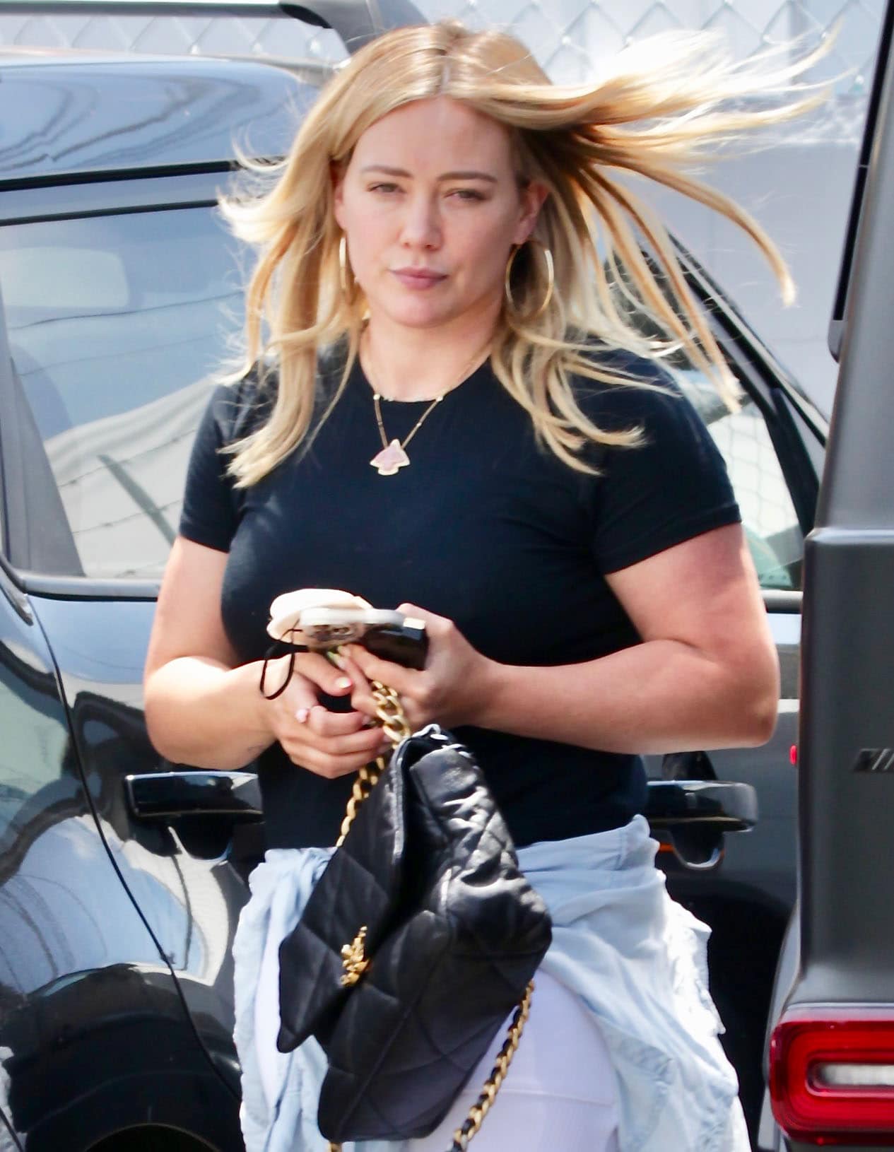 Hilary Duff styles her workout look with hoop earrings, a gold necklace, and a Chanel bag