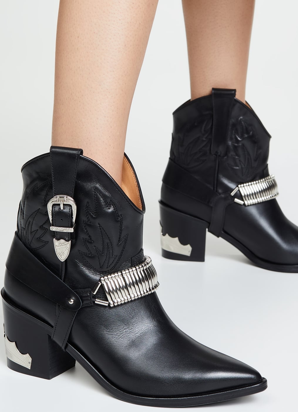 A boldly modern take on a classic cowboy boot, these black buckled booties add a harness strap and eye-catching hardware to a must-have Western style