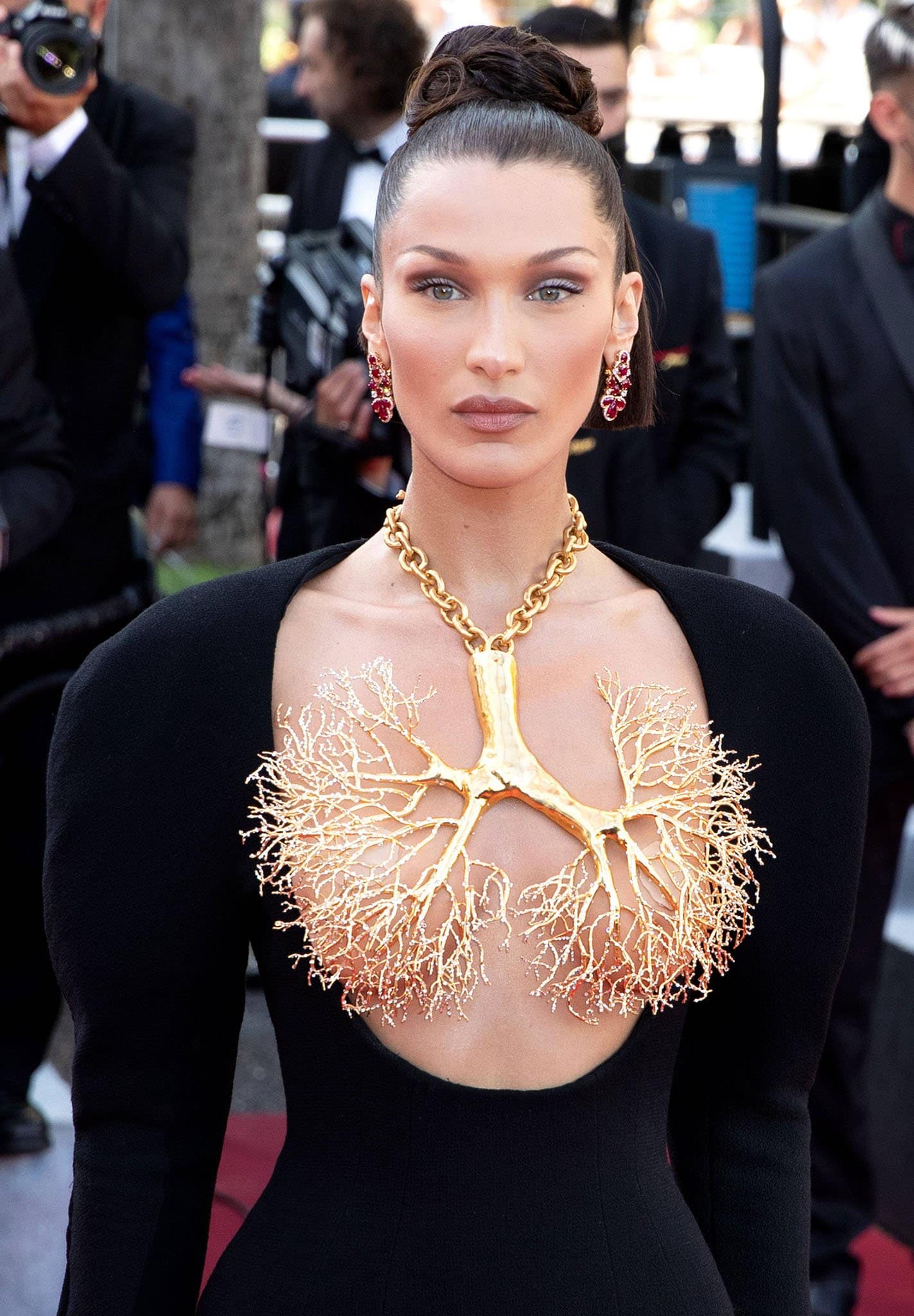 Wearing a gilded brass necklace of a human lung's pulmonary veins, Bella Hadid styles her tresses in an intricate updo and wears smokey eyeshadow with nude lipstick