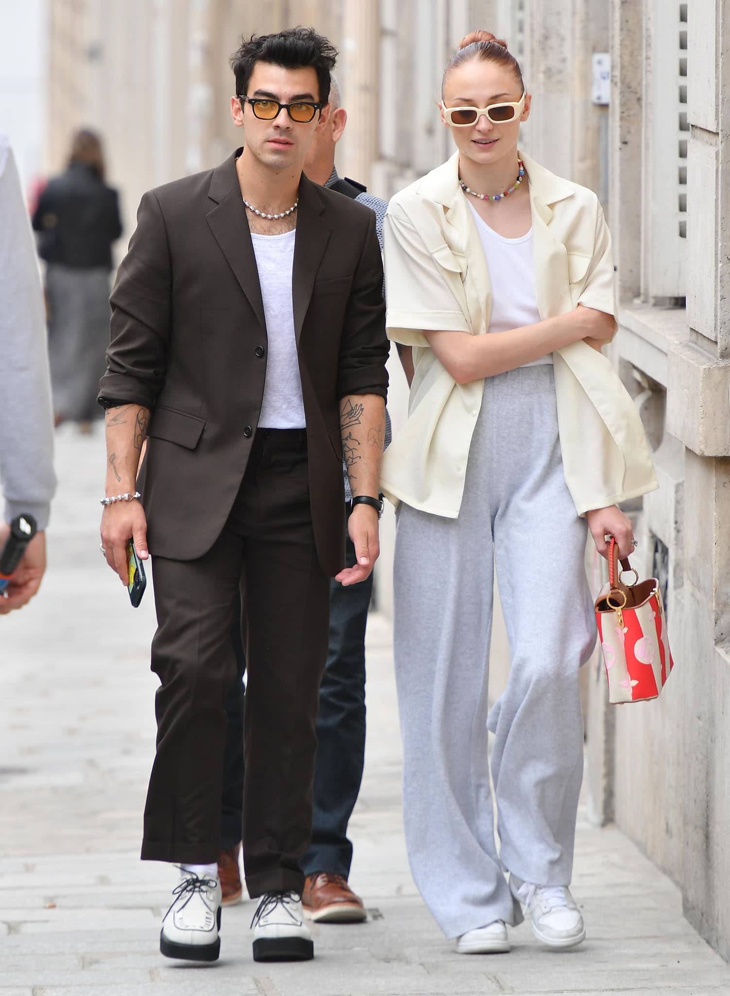 Joe Jonas looks handsome in his brown pantsuit with a white tee, brogues, and yellow-tinted sunglasses