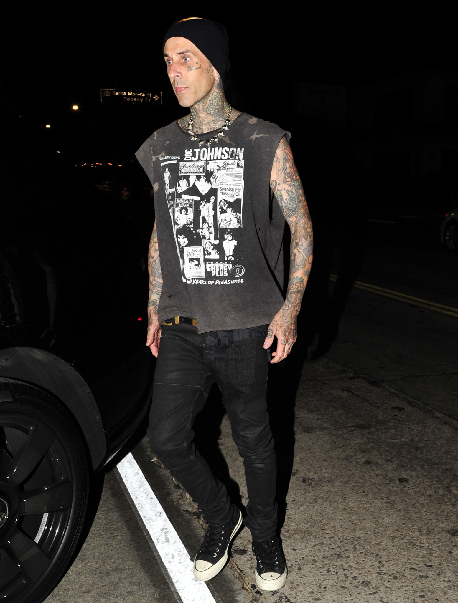 Blink 182 drummer Travis Barker shows off his body tattoos in a printed muscle tee, black jeans, and sneakers