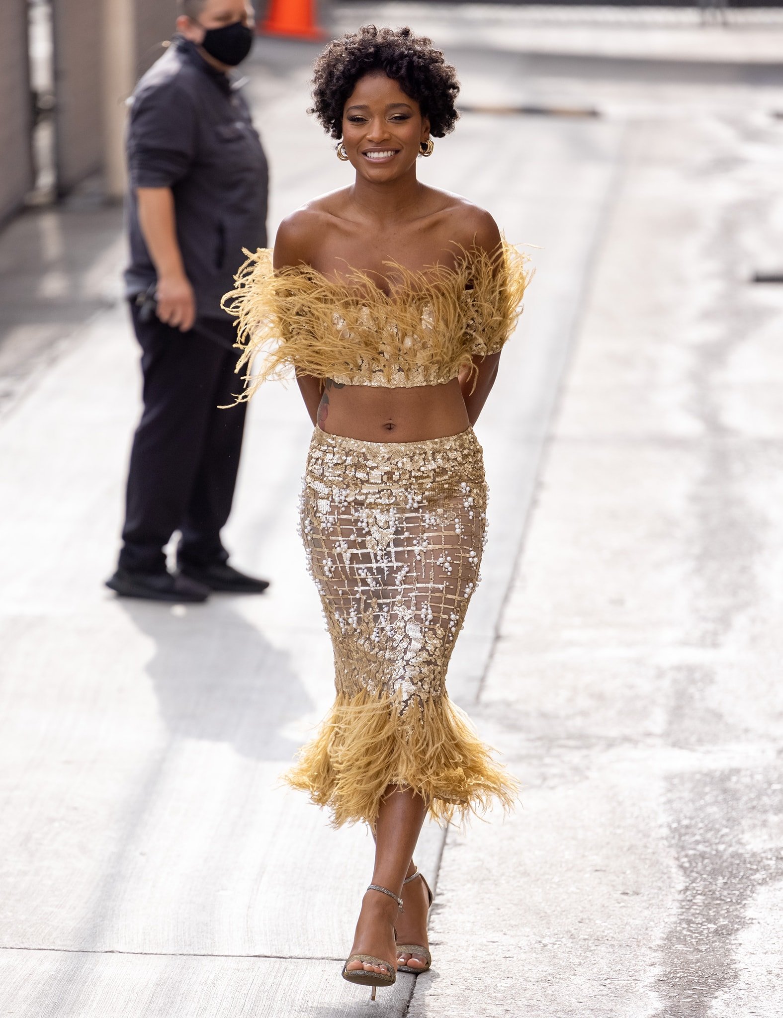 Keke Palmer's outfit features a gold sequined crop top and a matching mesh midi skirt with feather accents