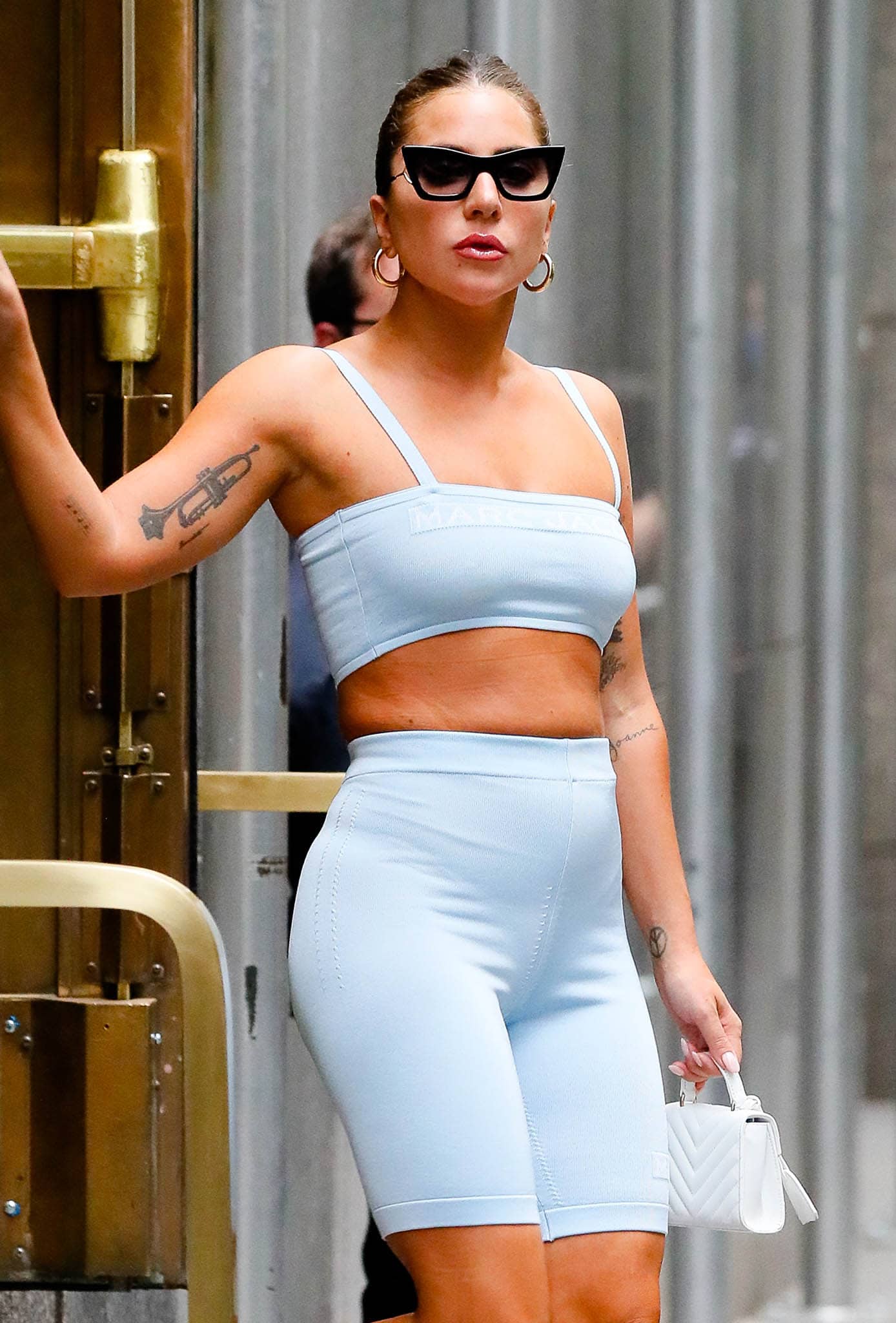 Lady Gaga wears a center-parted bun with Jennifer Fisher gold hoops and Mark Cross mini bag