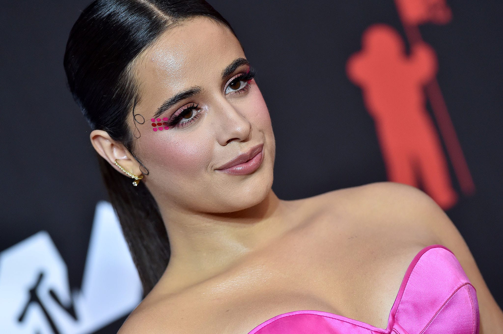 Camila Cabello wears a long, center-parted ponytail and bold makeup with colorful dots on the corner of her eyes