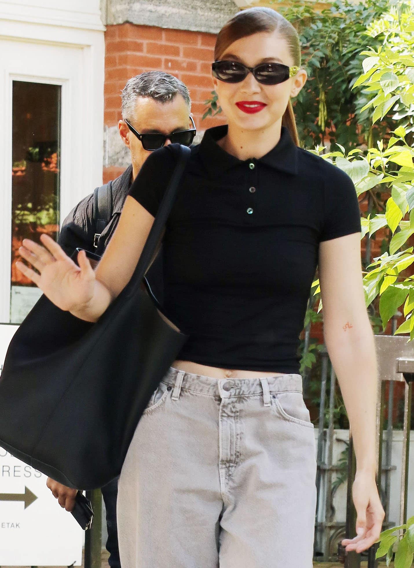 Gigi Hadid styles her hair in a slick side-parted ponytail and wears a swipe of bold red lipstick