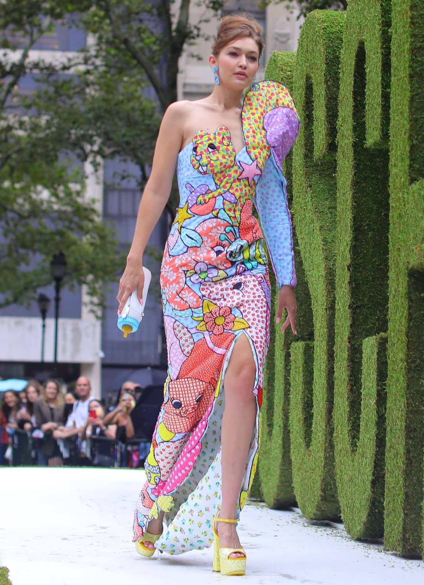 Gigi Hadid wears a pastel cartoon animal frock with yellow platform heels and a baby bottle clutch for Moschino's NYFW runway show on September 9, 2021