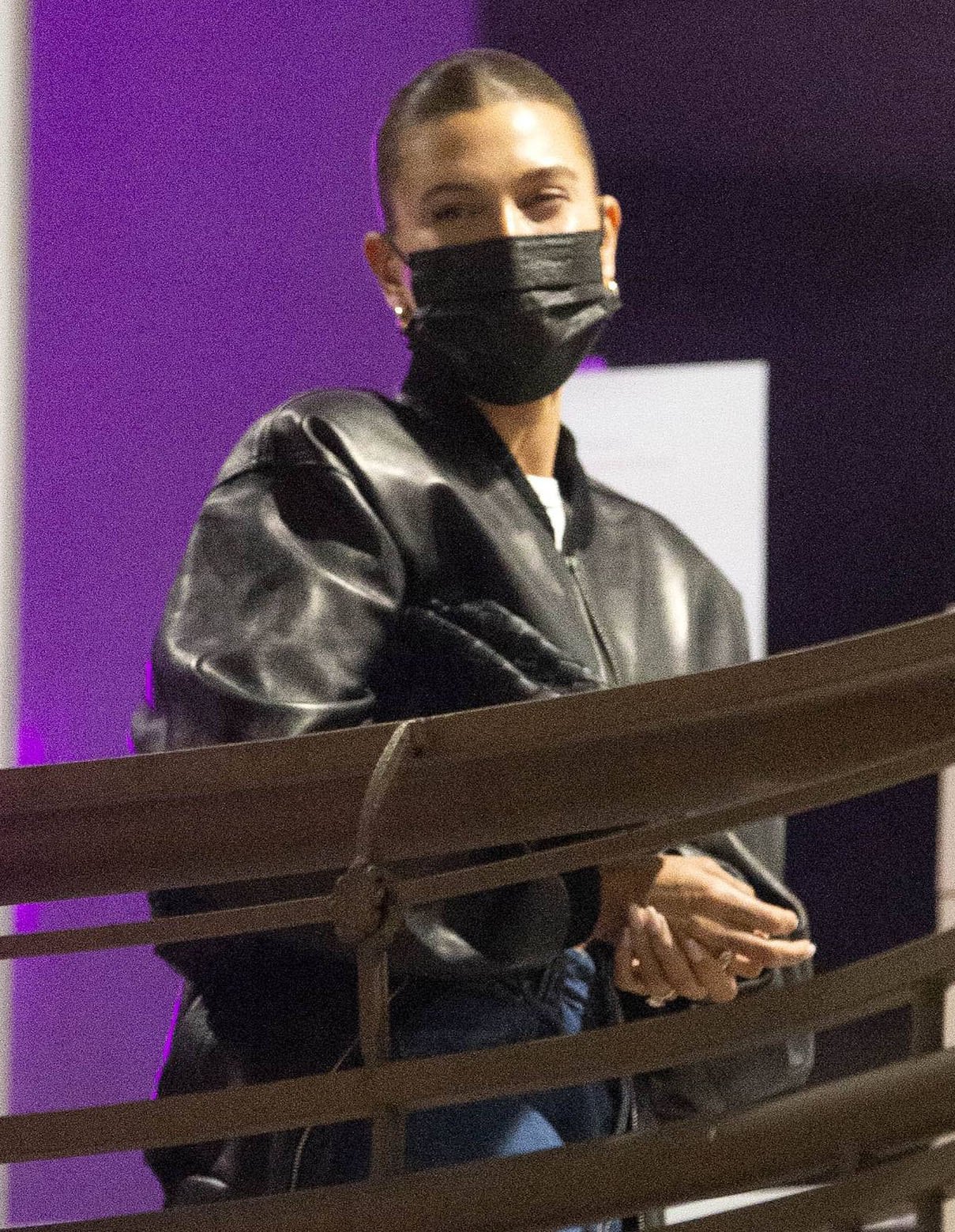 Hailey Bieber wears her signature sleek bun hairstyle and covers her face with a black face mask