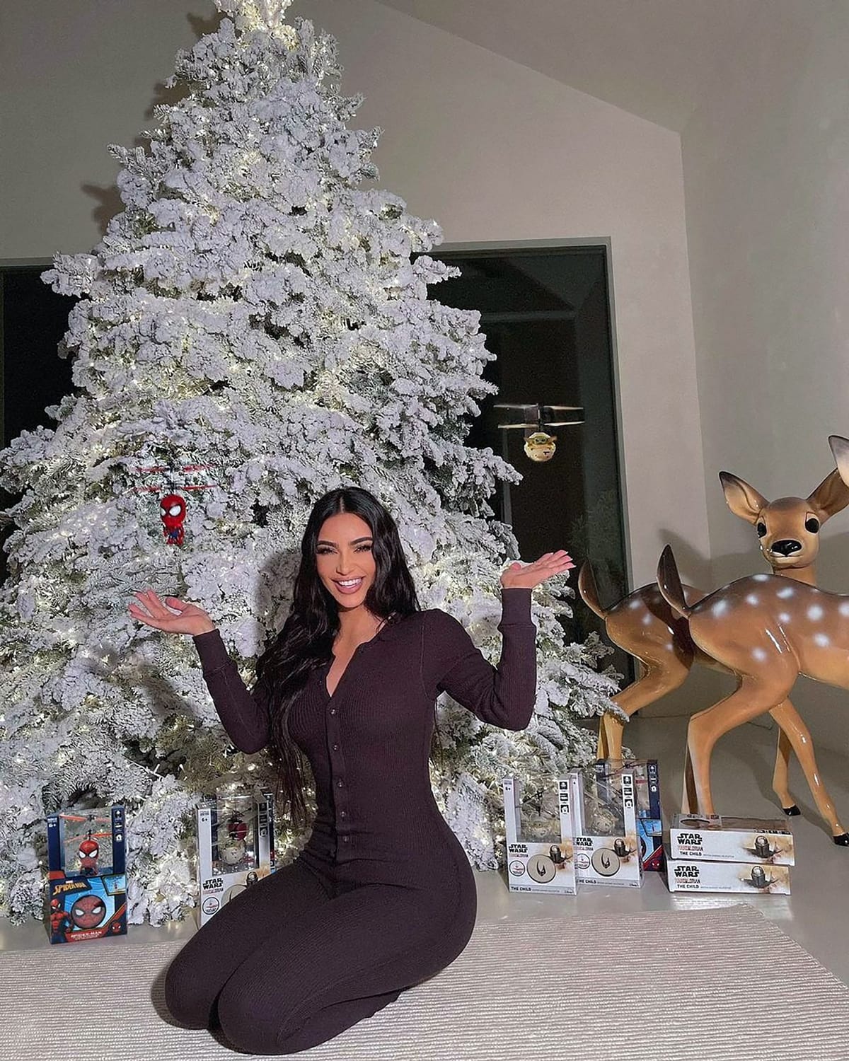 Kim Kardashian in a brown onesie with buttons from Skims posing with a Christmas as she offers parents advice on Christmas shopping for kids' presents