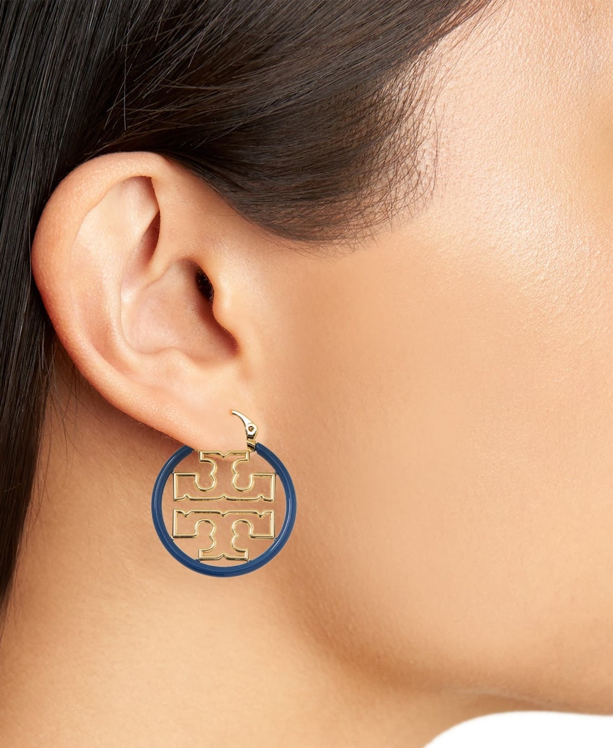 Smooth enamel surrounds glinting double-T logos in these small blue and gold hoop earrings from Tory Burch