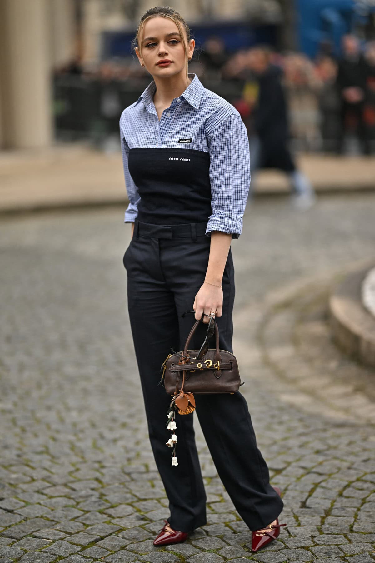 Joey King exudes effortless Parisian chic at the Miu Miu Fall/Winter 2025 show on March 11, 2025, pairing tailored trousers with a layered shirt-and-bustier combo, Miu Miu patent leather slingbacks and the brand’s Mini Aventure tote for a polished, modern edge