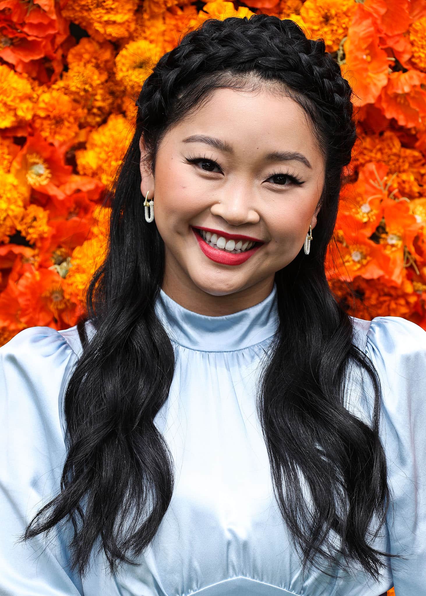 Lana Condor wears red lipstick and styles her hair in soft waves with a crown braid