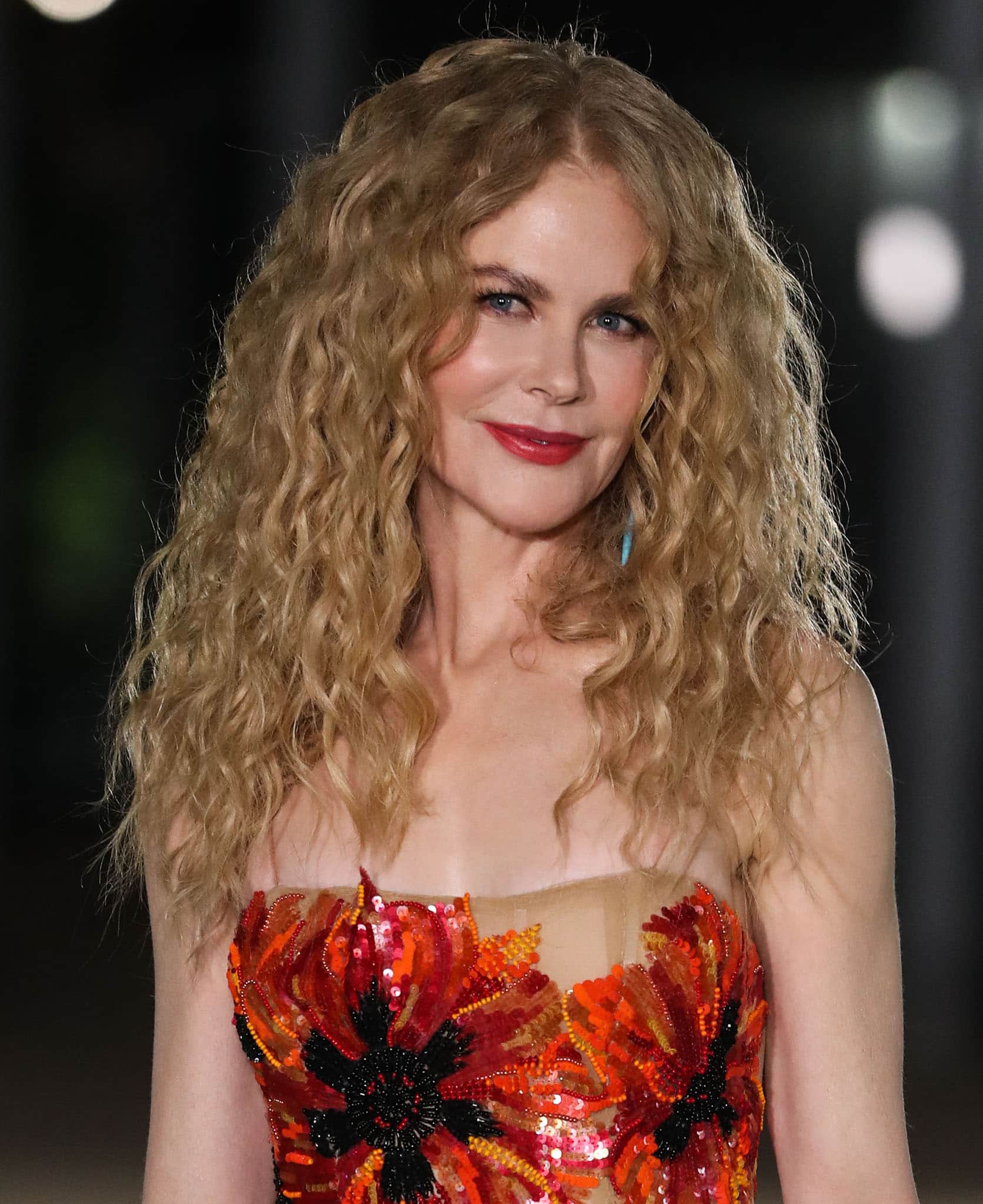Nicole Kidman enhances her natural beauty with voluminous, frizz-free curls, complemented by dewy makeup featuring a bold red lip and soft eyeliner for a glamorous yet effortless look