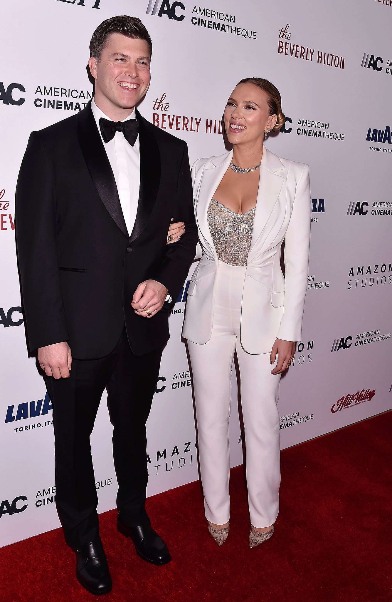 Tuxedo-clad Colin Jost accompanies wife Scarlett Johansson, who wows in a custom Versace white suit and crystal-embellished bustier top
