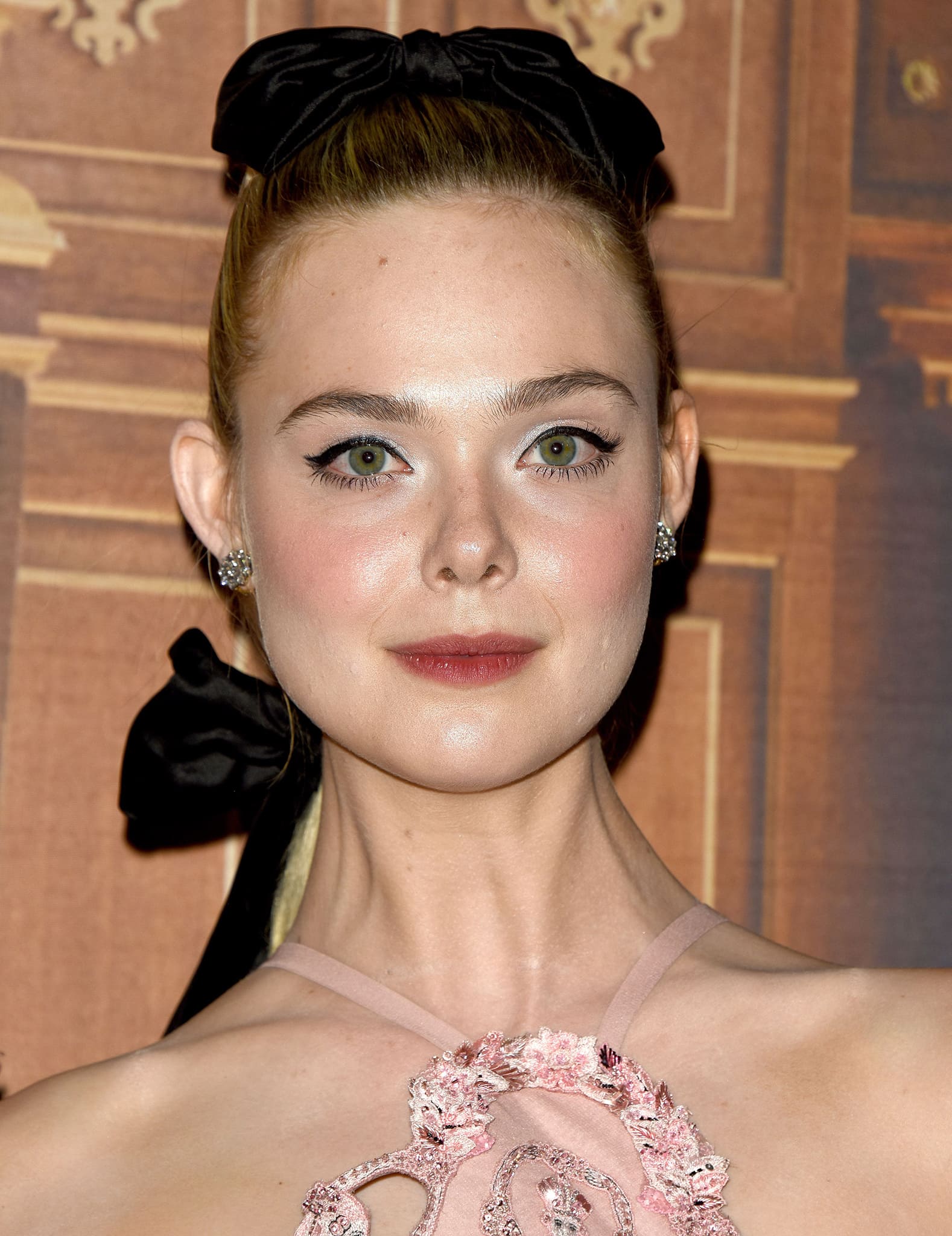Elle Fanning pulls her tresses in a ponytail with black bow accents and wears winged eyeliner with red lipstick