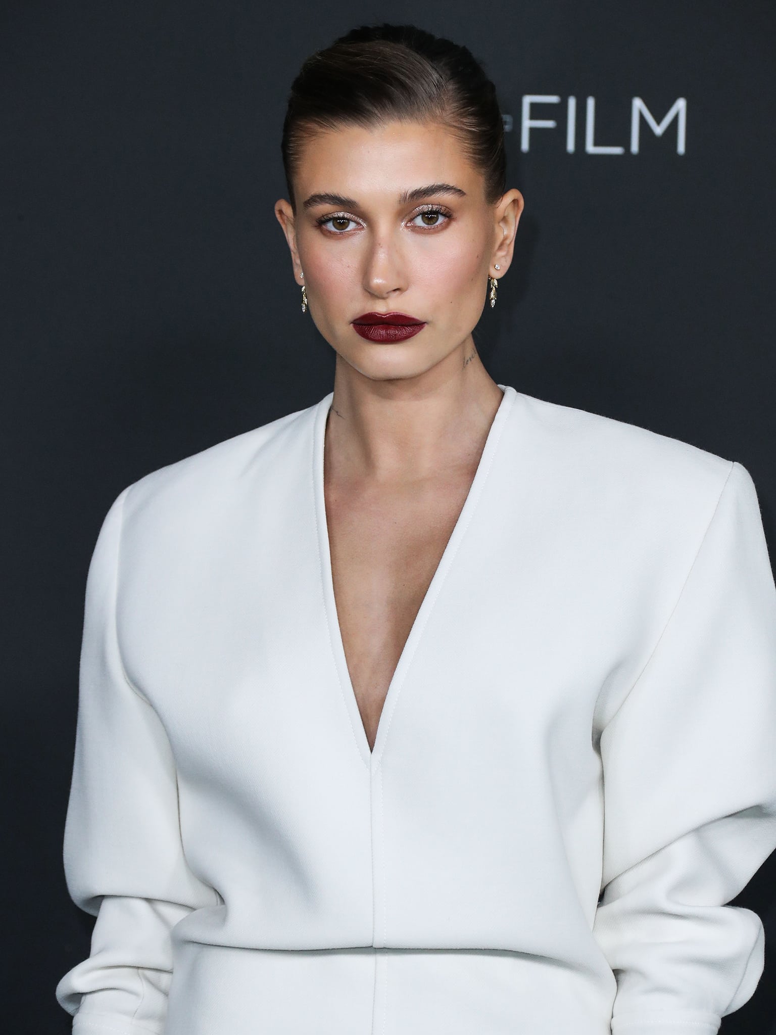 Hailey Bieber wears minimal makeup with bold maroon lipstick and shimmering eyeshadow