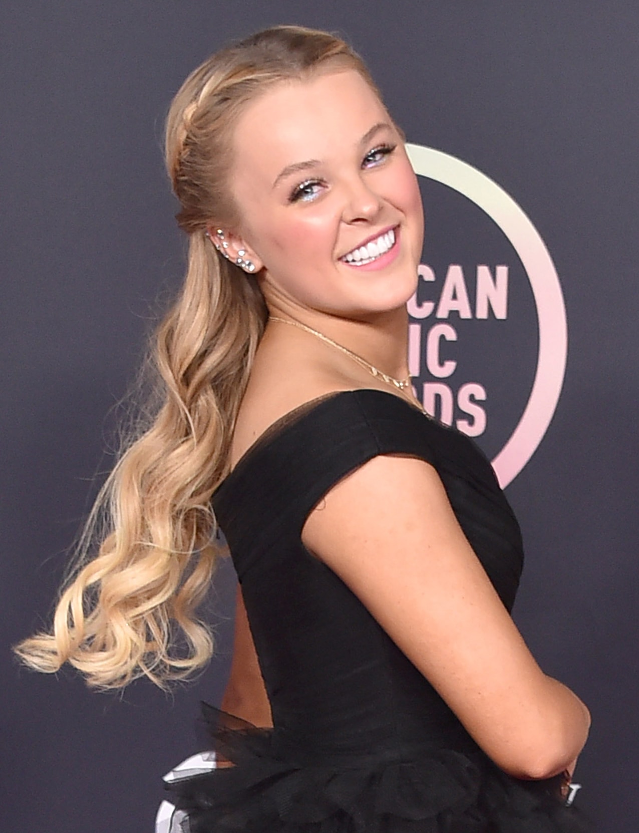 Jojo Siwa trades her ponytail for a wavy half-up, half-down hairstyle with glittery eyeshadow and soft pink lipstick