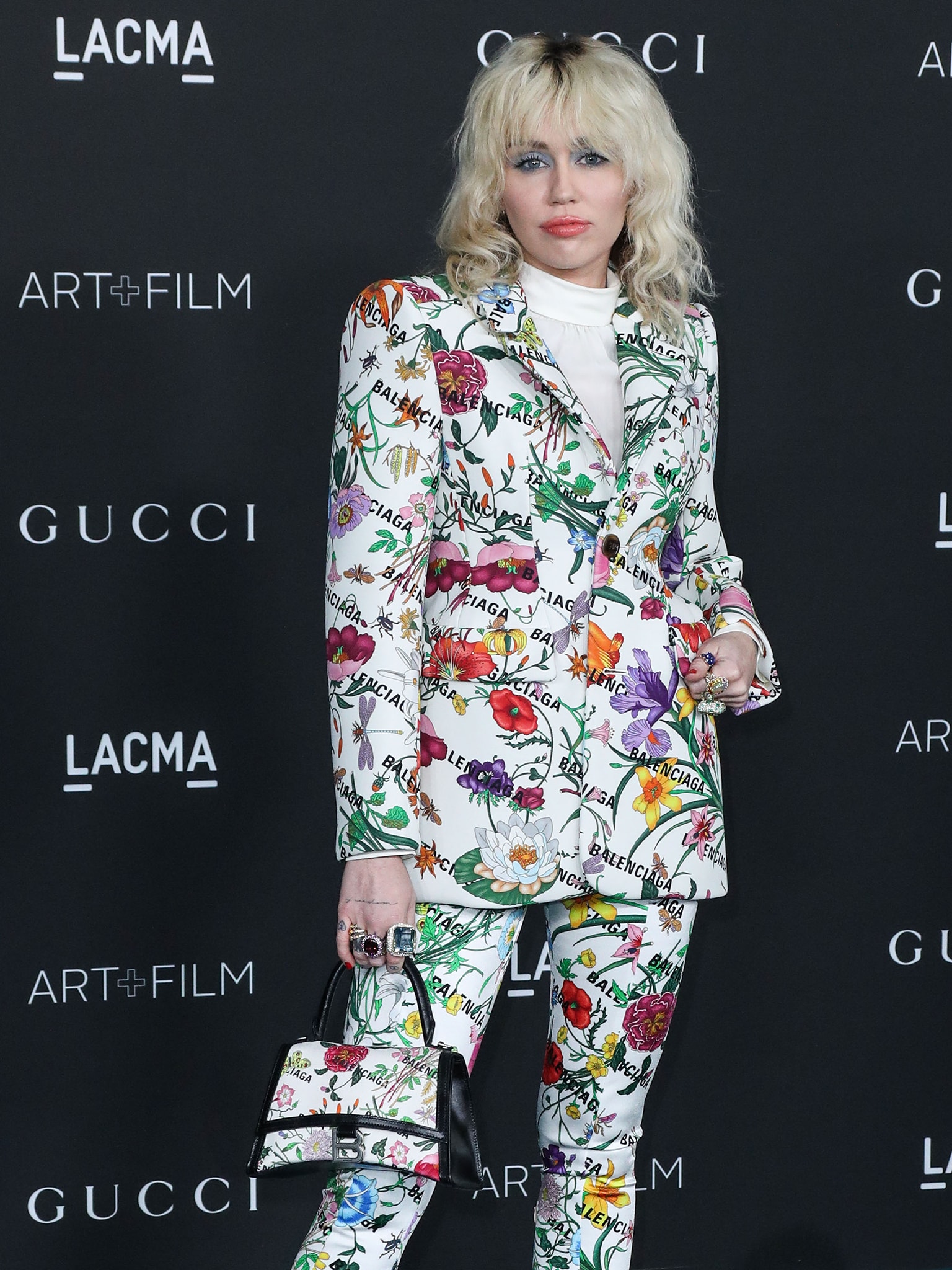 Miley Cyrus styles her look with a matching handbag and a slew of large statement rings