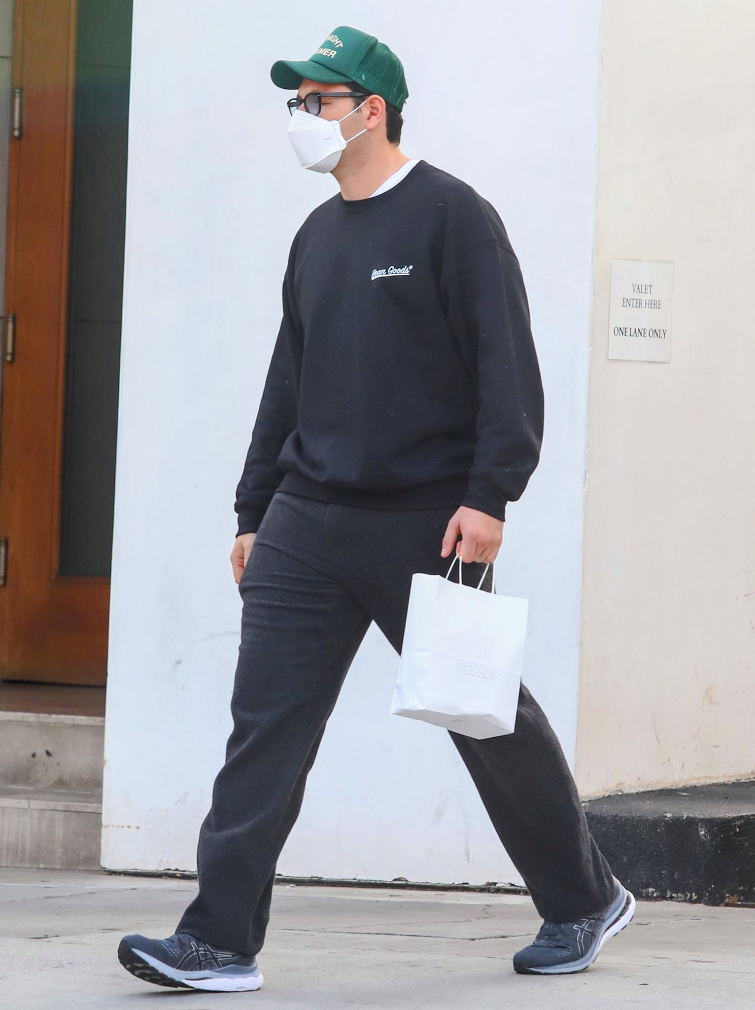 Elliot Grainge dons a black sweater, black pants, and navy Asics sneakers