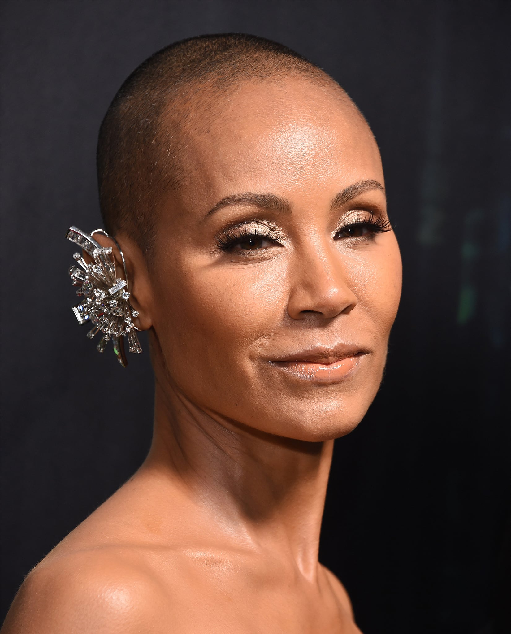 Jada Pinkett Smith wears buzz-cut hair and neutral makeup and adds edge to her look with a Swarovski ear cuff
