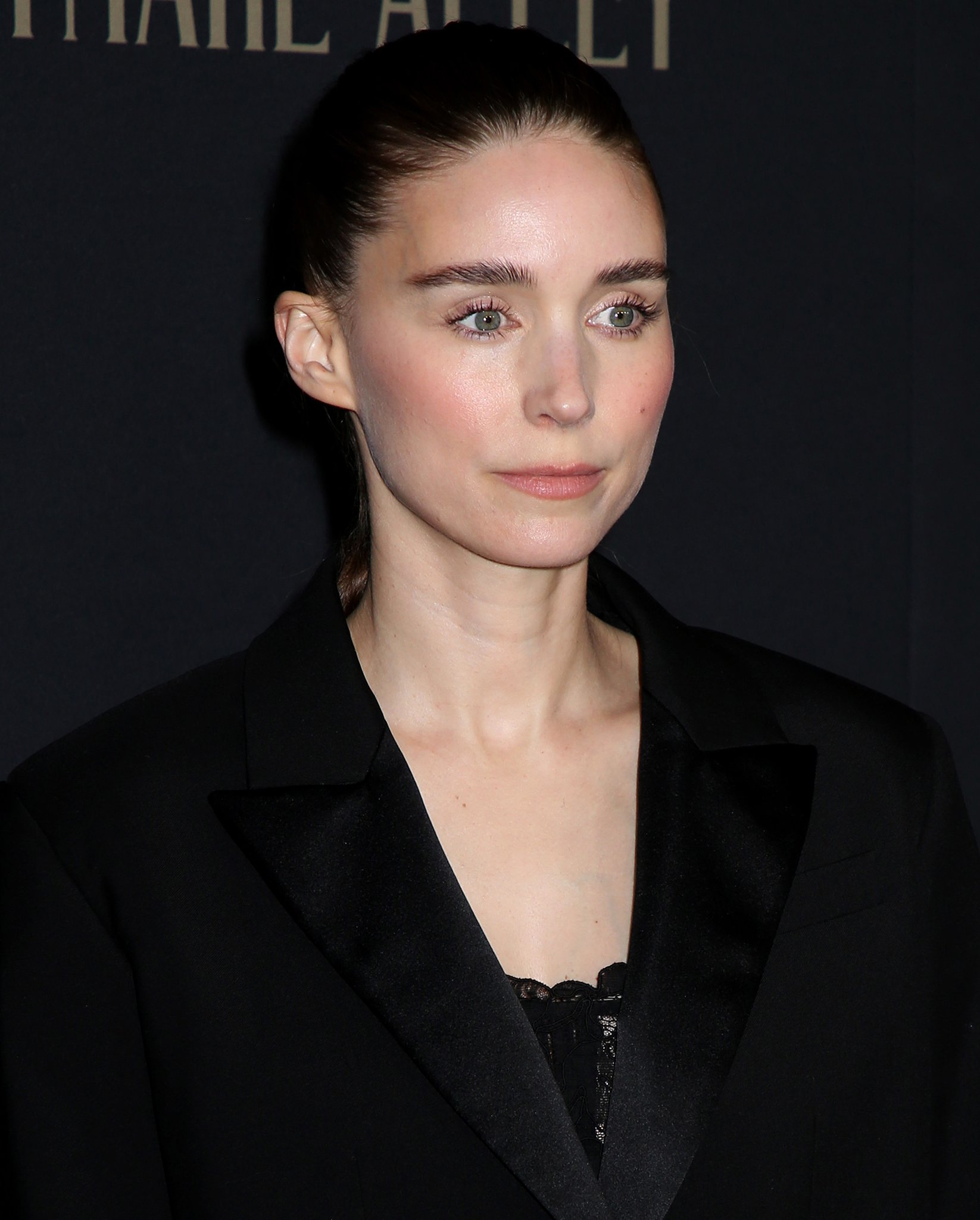 Rooney Mara wears a neat bun with brushed up brows, coral pink lipstick, blush, and mascara
