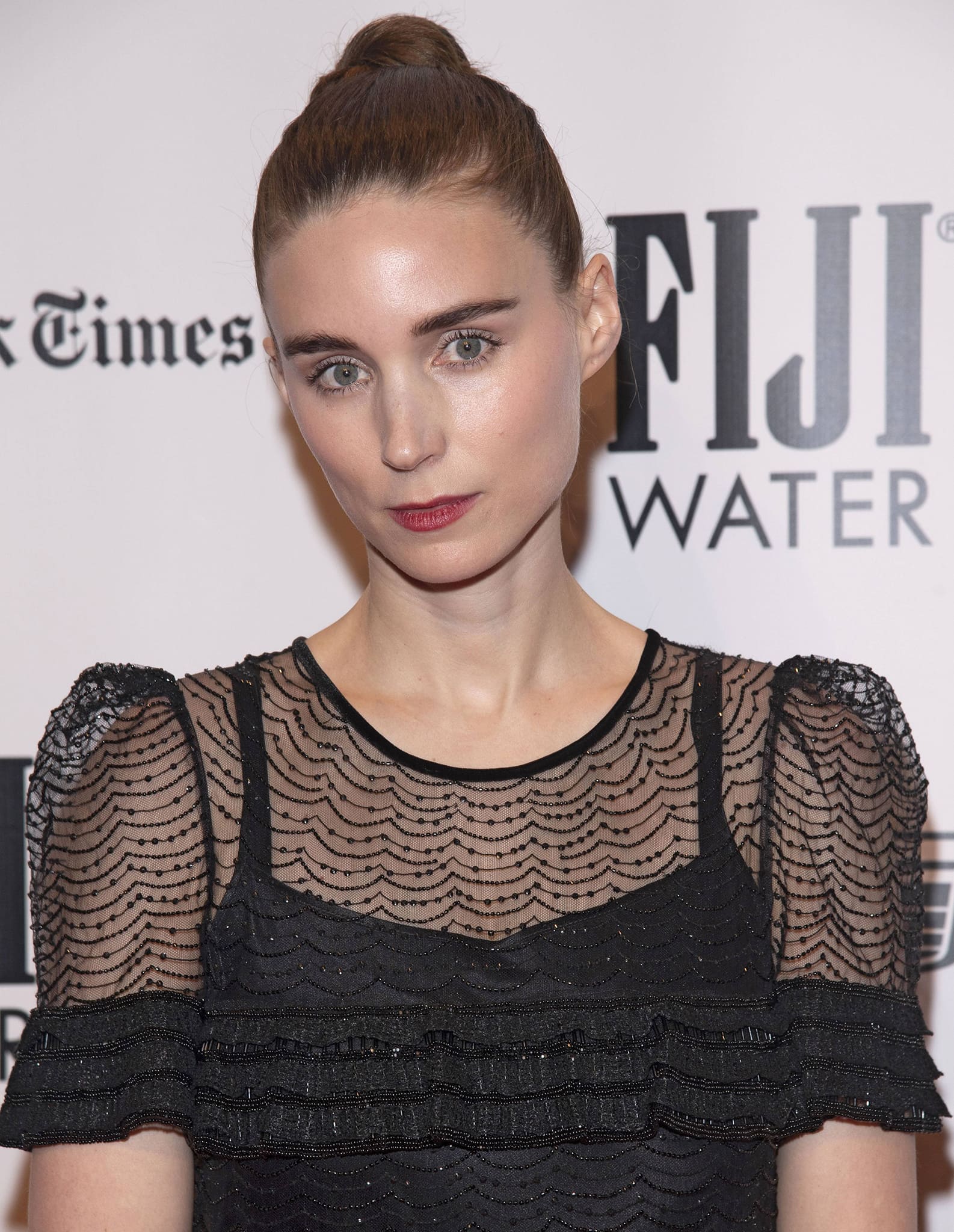 Rooney Mara wears a tight bun and highlights her features with mascara, blush, and red lipstick