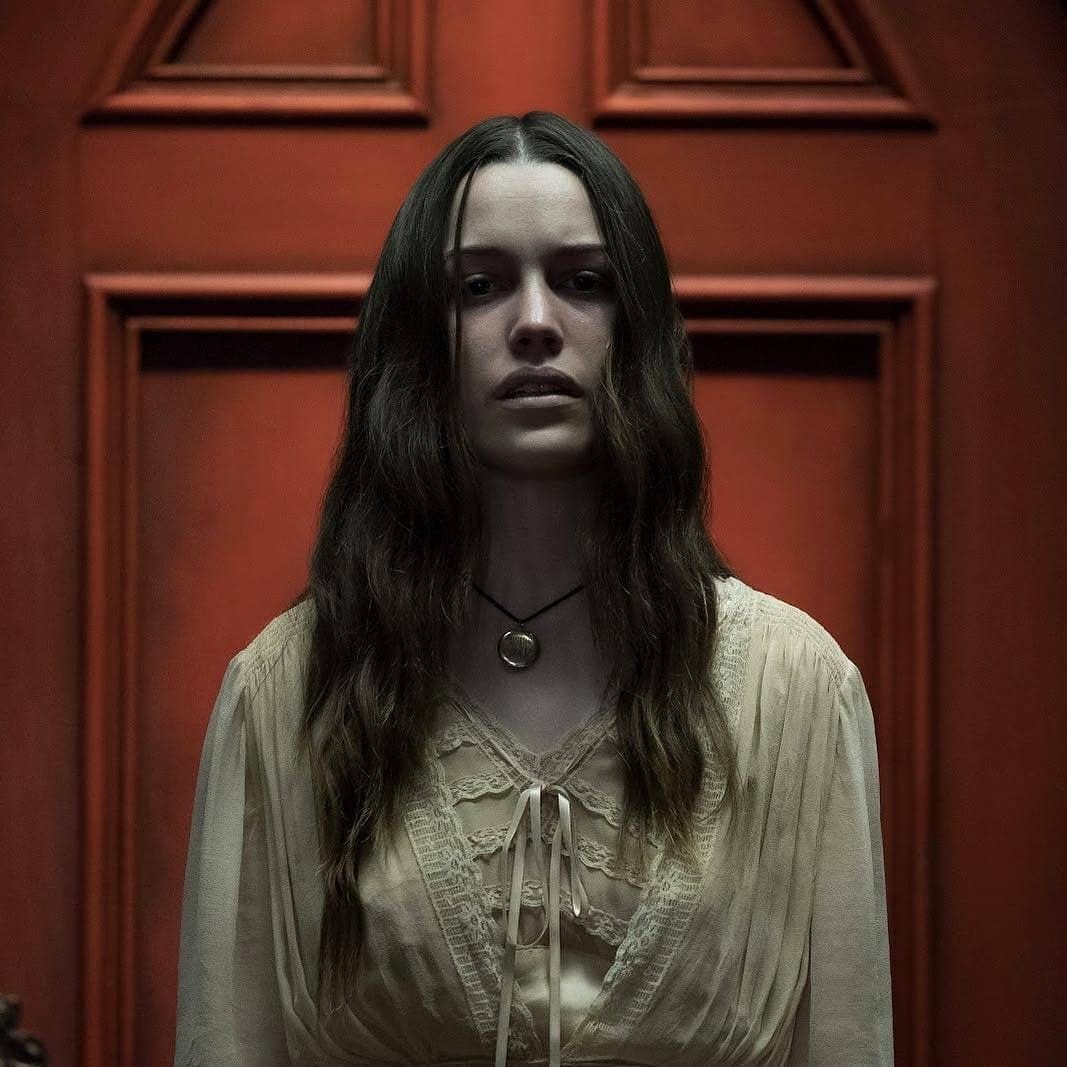Victoria Pedretti as Nell Crain in The Haunting of Hill House, standing before the iconic red door in a chilling scene from the Netflix series