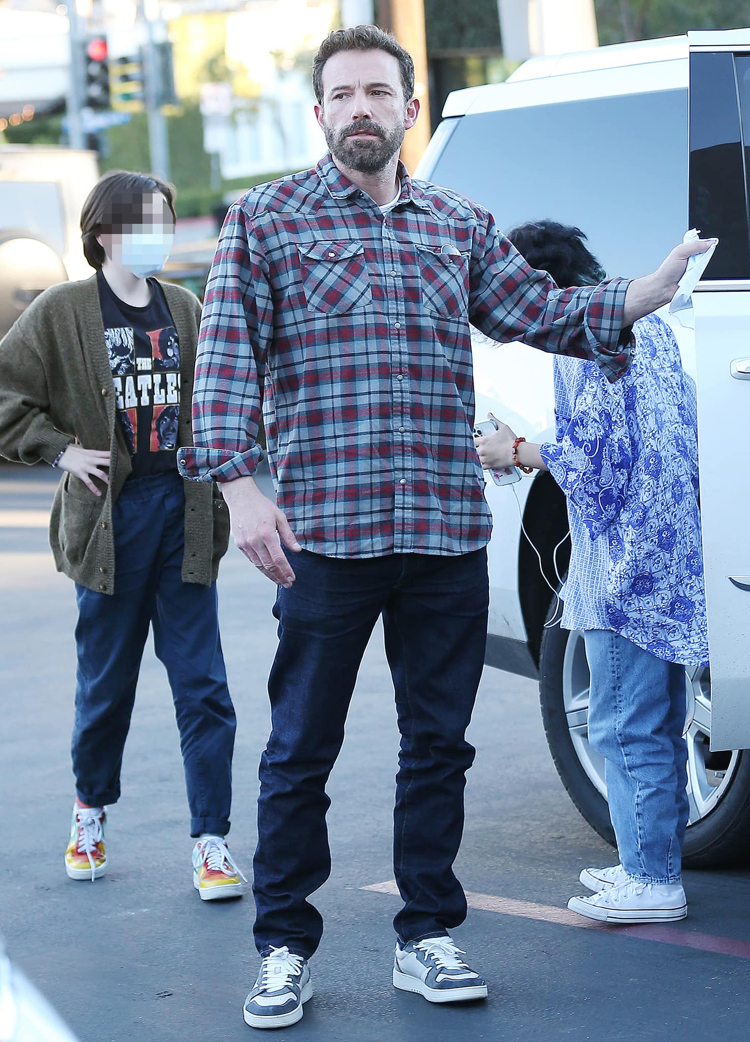 Ben Affleck wears a plaid flannel shirt with blue jeans and casual sneakers