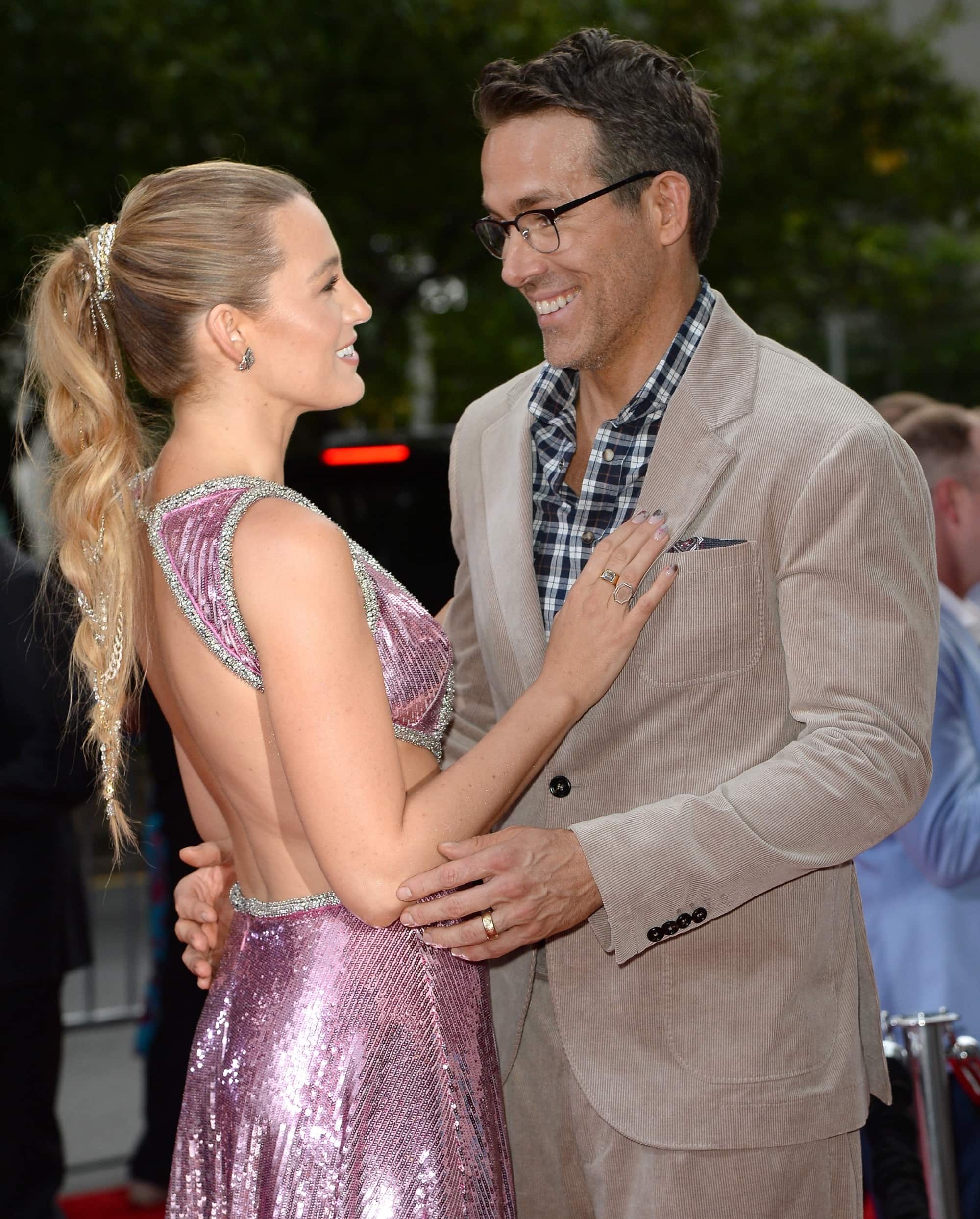 Blake Lively and Ryan Reynolds share a sweet moment on the red carpet, with Blake sparkling in a stunning backless pink gown and Ryan keeping it stylish in a casual yet sophisticated beige suit