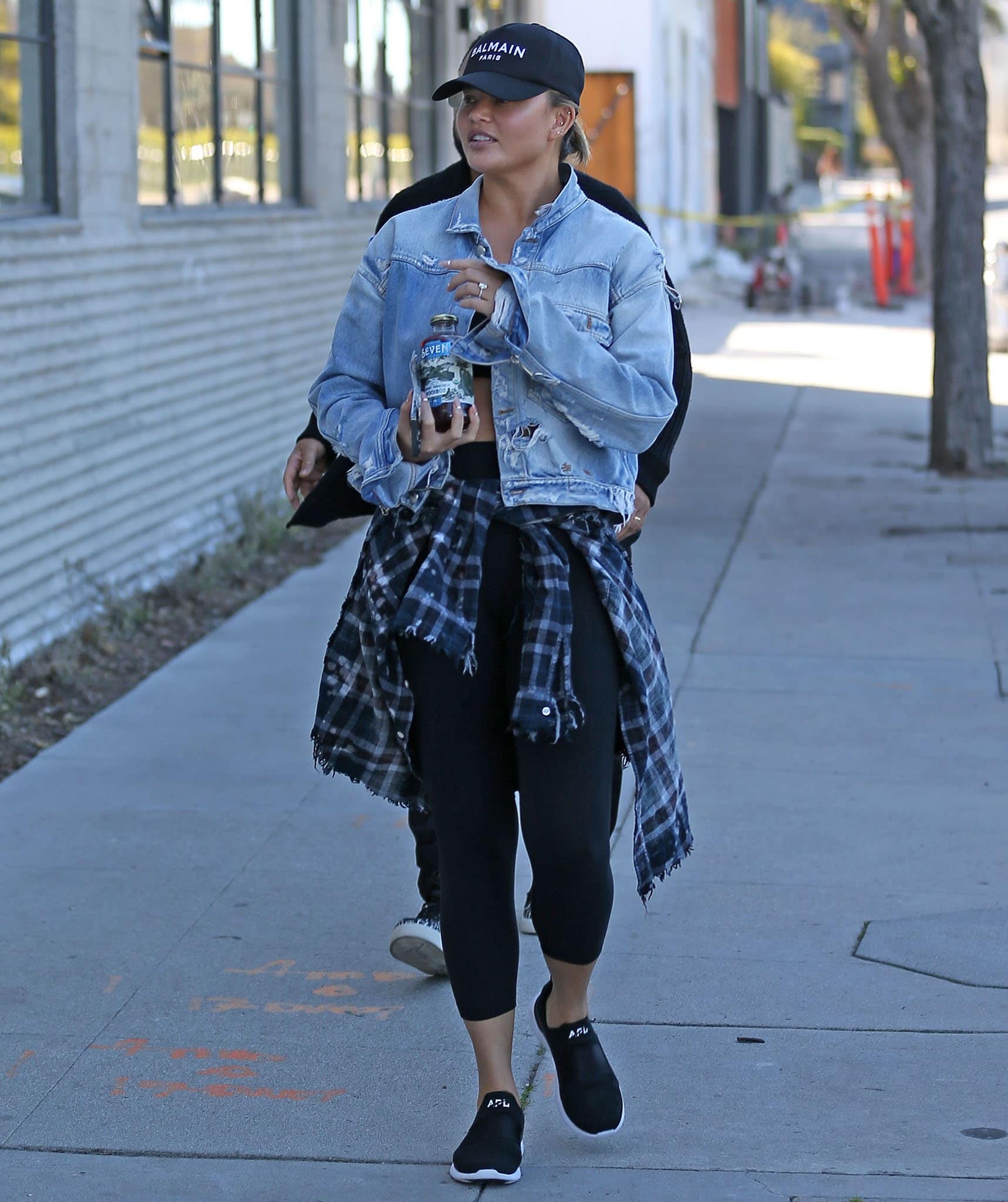 Chrissy Teigen gets sporty in bandeau top and leggings, styled with an R13 distressed denim jacket and a plaid shirt