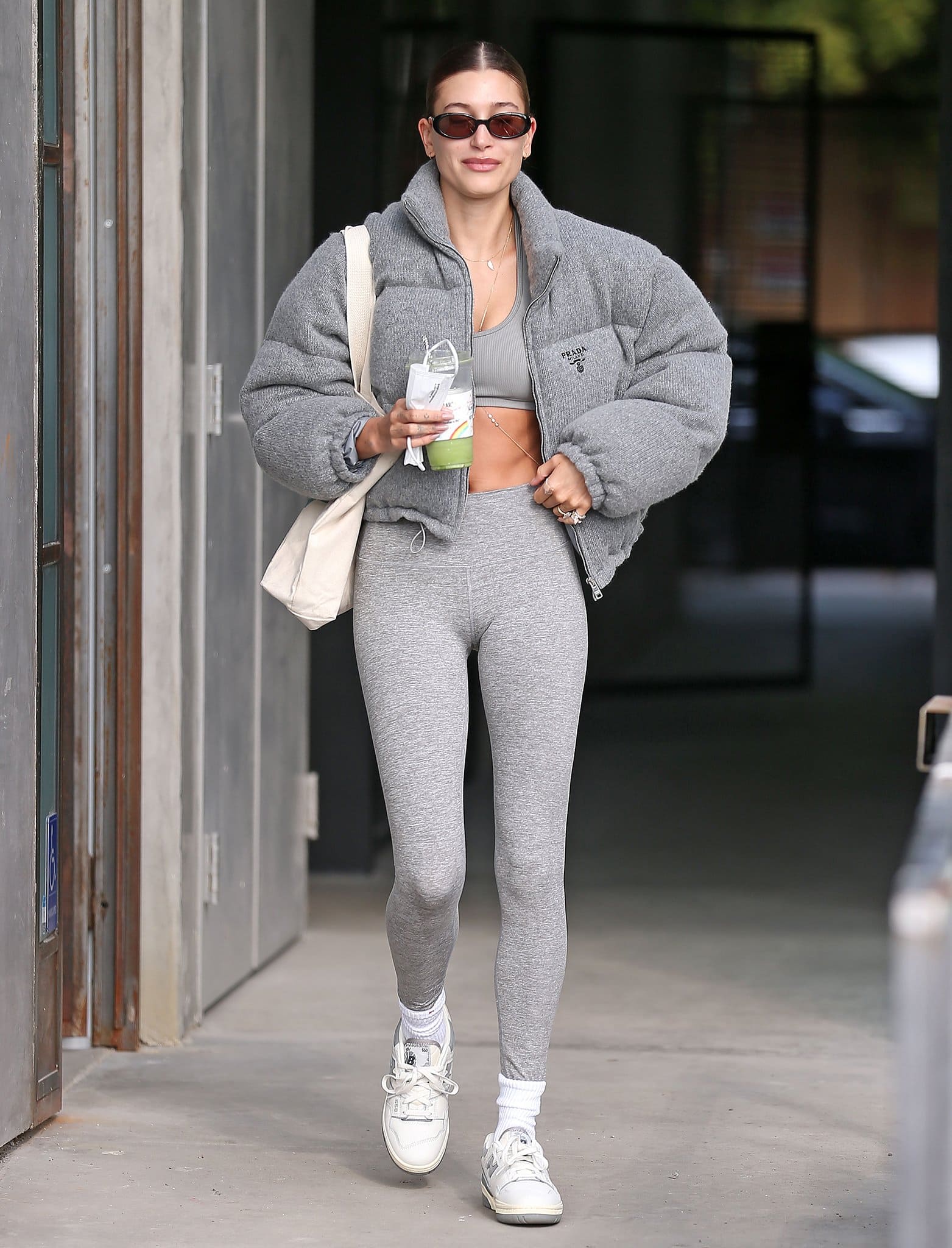Hailey Bieber shows her abs in monochrome gray activewear with a Prada puffer jacket