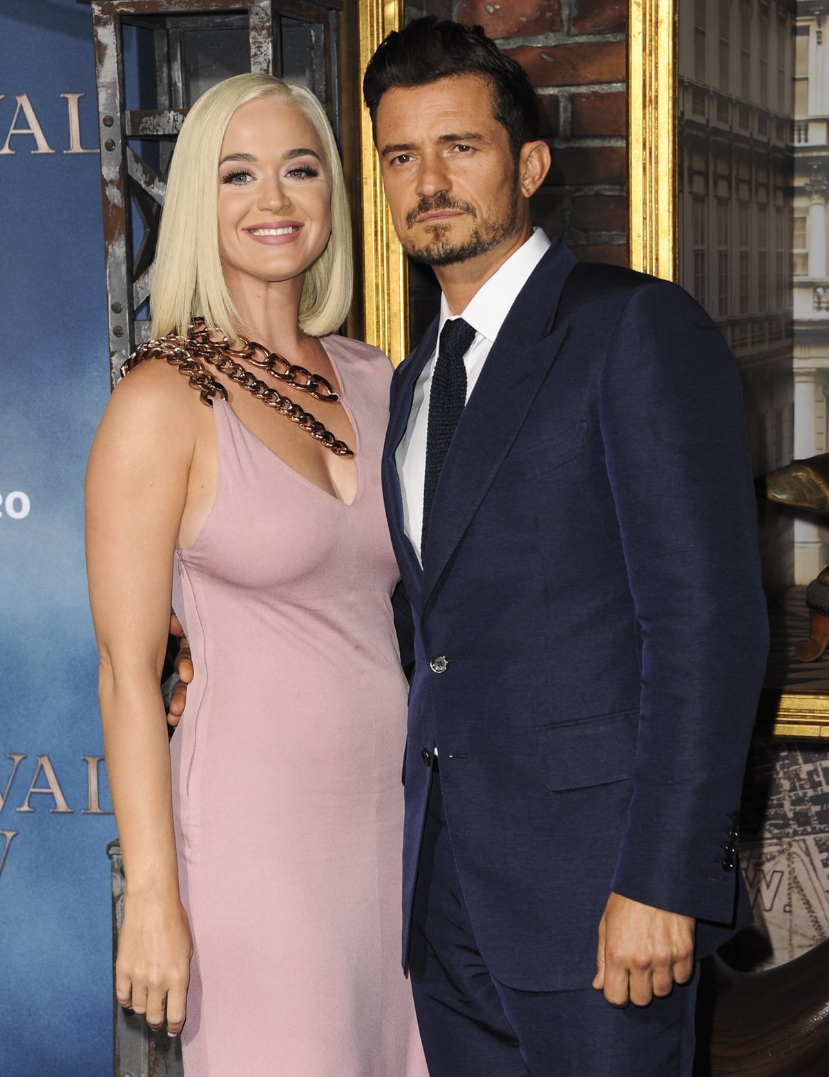 Katy Perry looks radiant in a blush pink gown with bold chain detailing, while Orlando Bloom exudes sophistication in a sharp navy suit