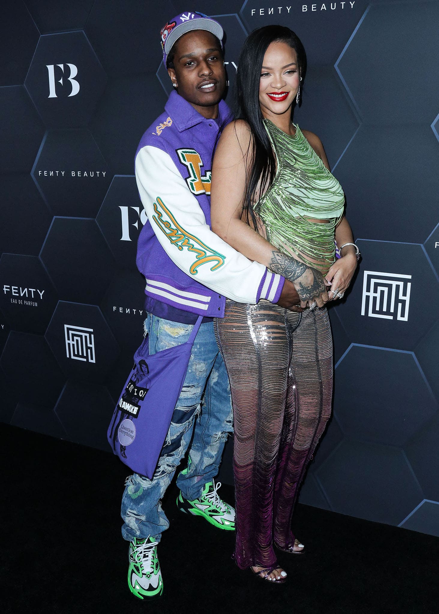 A$AP Rocky hugs pregnant Rihanna from behind in Louis Vuitton purple jacket, loose jeans, and green sneakers