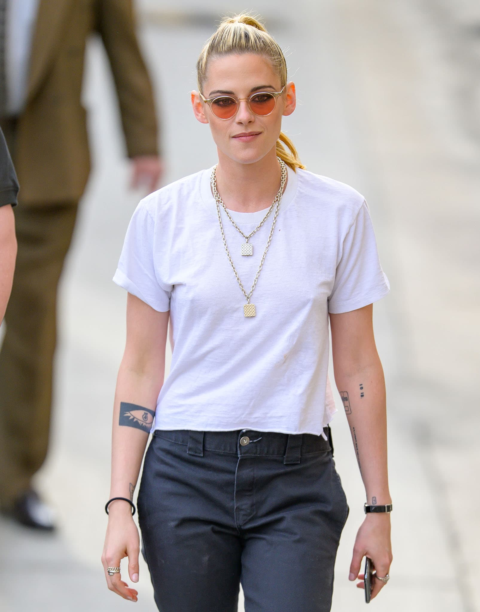Kristen Stewart ties her hair back and styles her casual outfit with chain necklaces and tinted sunglasses