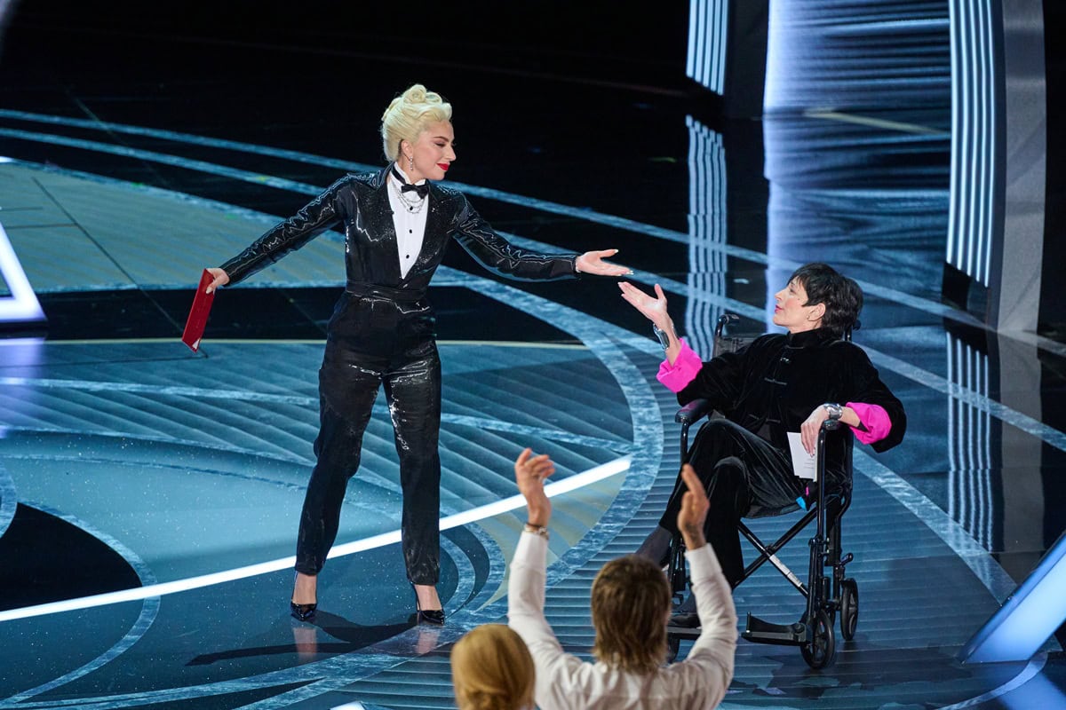 Lady Gaga joins Liza Minnelli onstage at the Oscars to present Best Picture, wearing a Ralph Lauren liquid lamé tuxedo jumpsuit with Jimmy Choo Romy heels and Tiffany & Co. diamond jewelry
