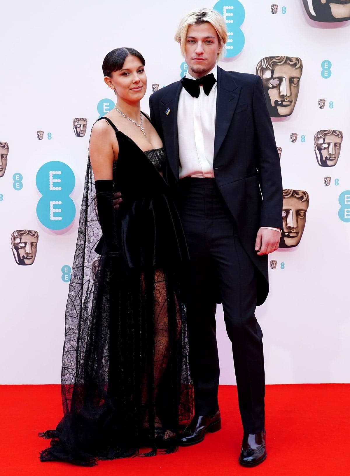 Millie Bobby Brown and boyfriend Jake Bongiovi made their red-carpet debut at the 2022 EE British Academy Film Awards on March 13, 2022, where she stunned in a custom Louis Vuitton velvet-and-lace gown paired with towering, barely visible Giuseppe Zanotti platform sandals beneath the hem