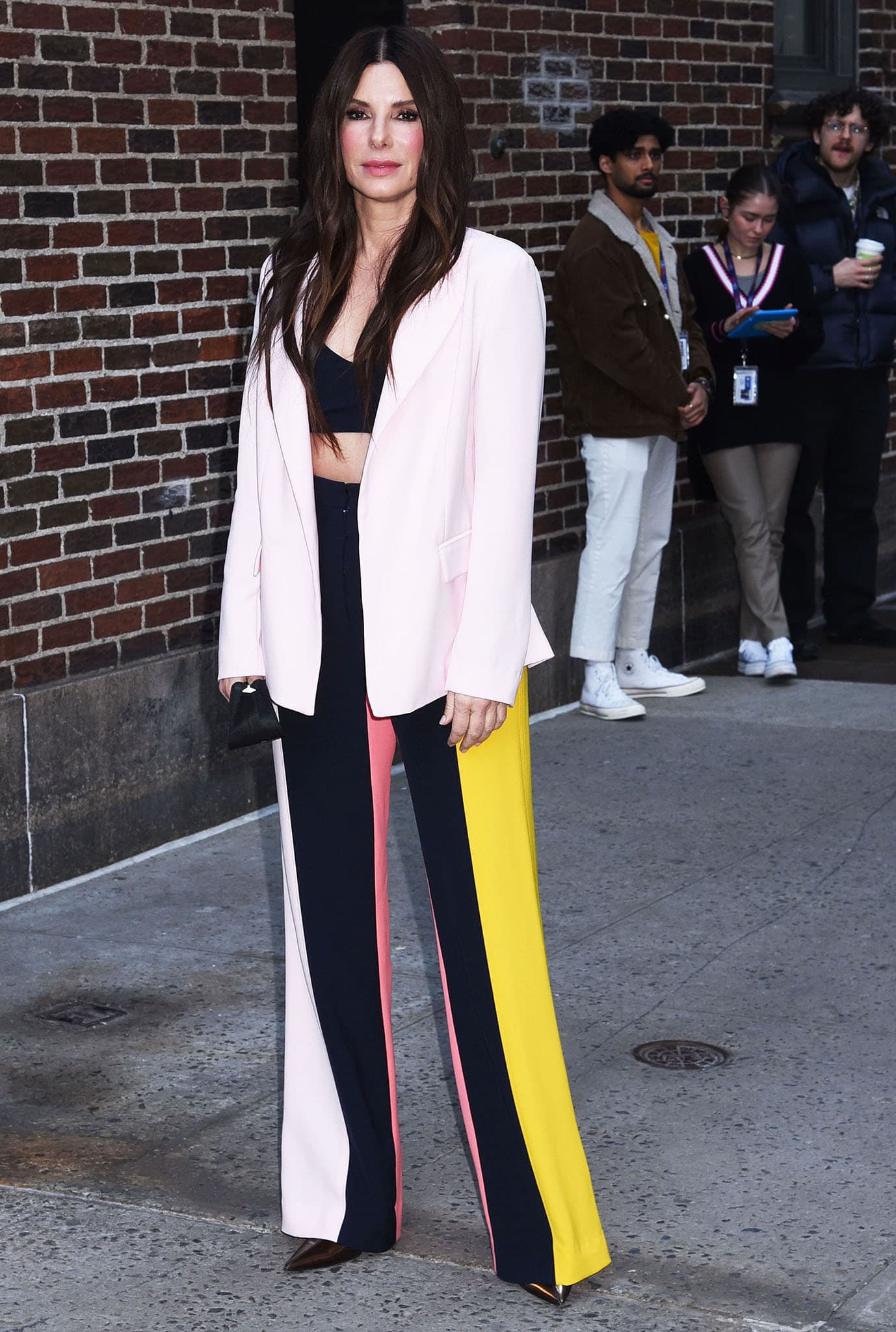 Sandra Bullock flashes her abs and cleavage in a navy bralette and a pair of Lela Rose multicolored striped pants ahead of her appearance on The Late Show with Stephen Colbert