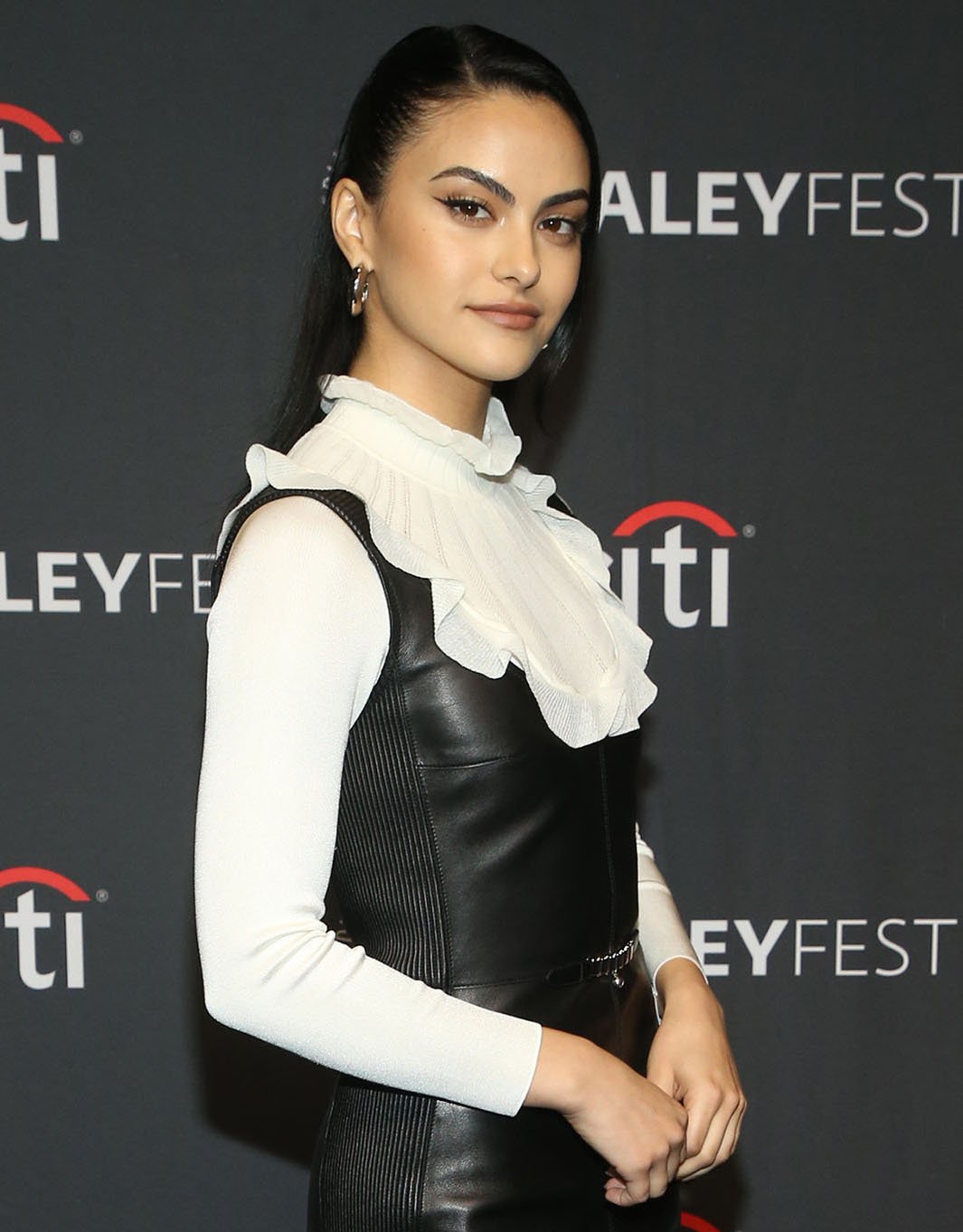 Camila Mendes styles her black hair in a half-up ponytail and wears winged eyeliner with nude eyeshadow and lipstick