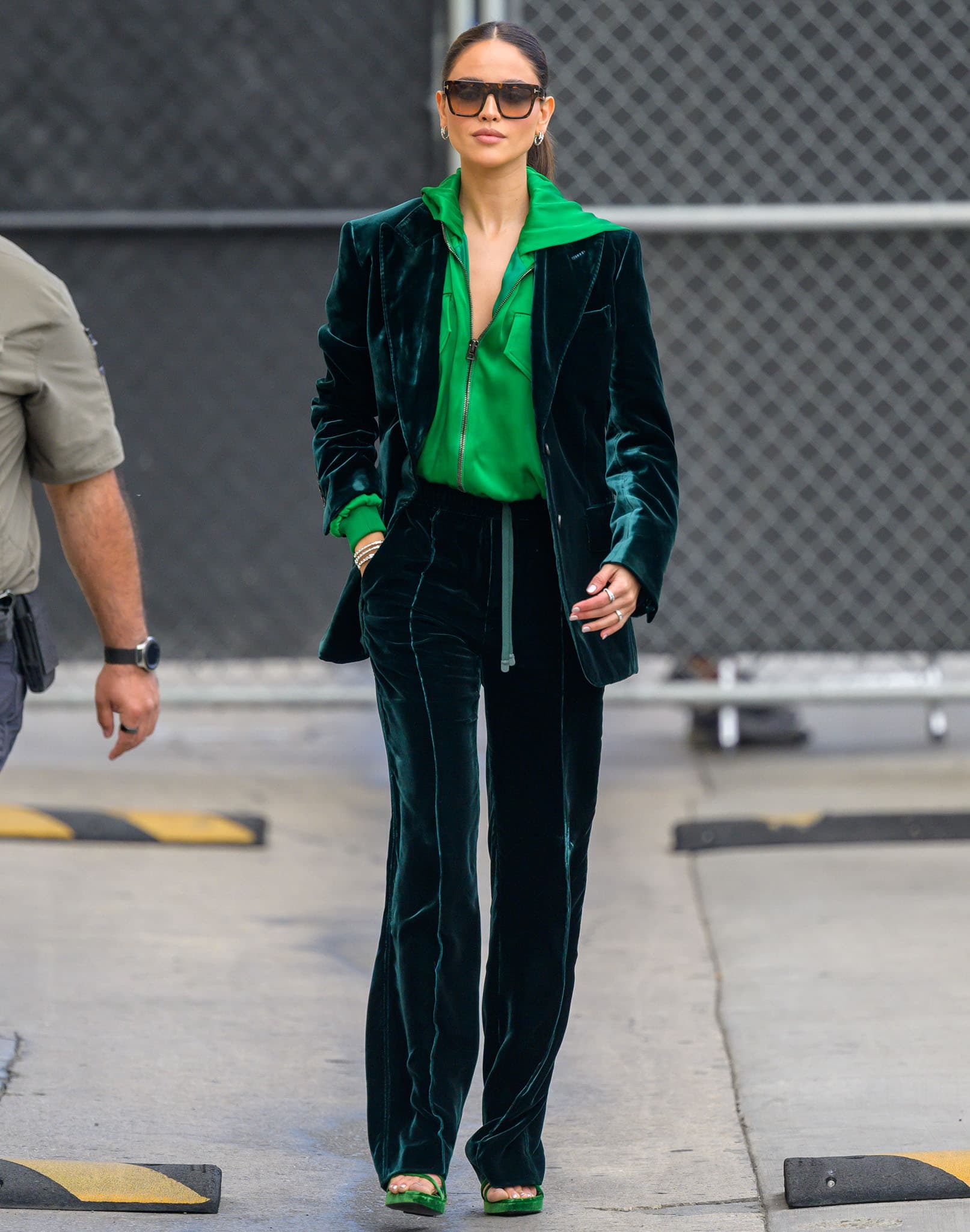 Eiza Gonzalez embraces monochromatic trend in a green velvet suit, a neon green hoodie, and a pair of green velvet sandals