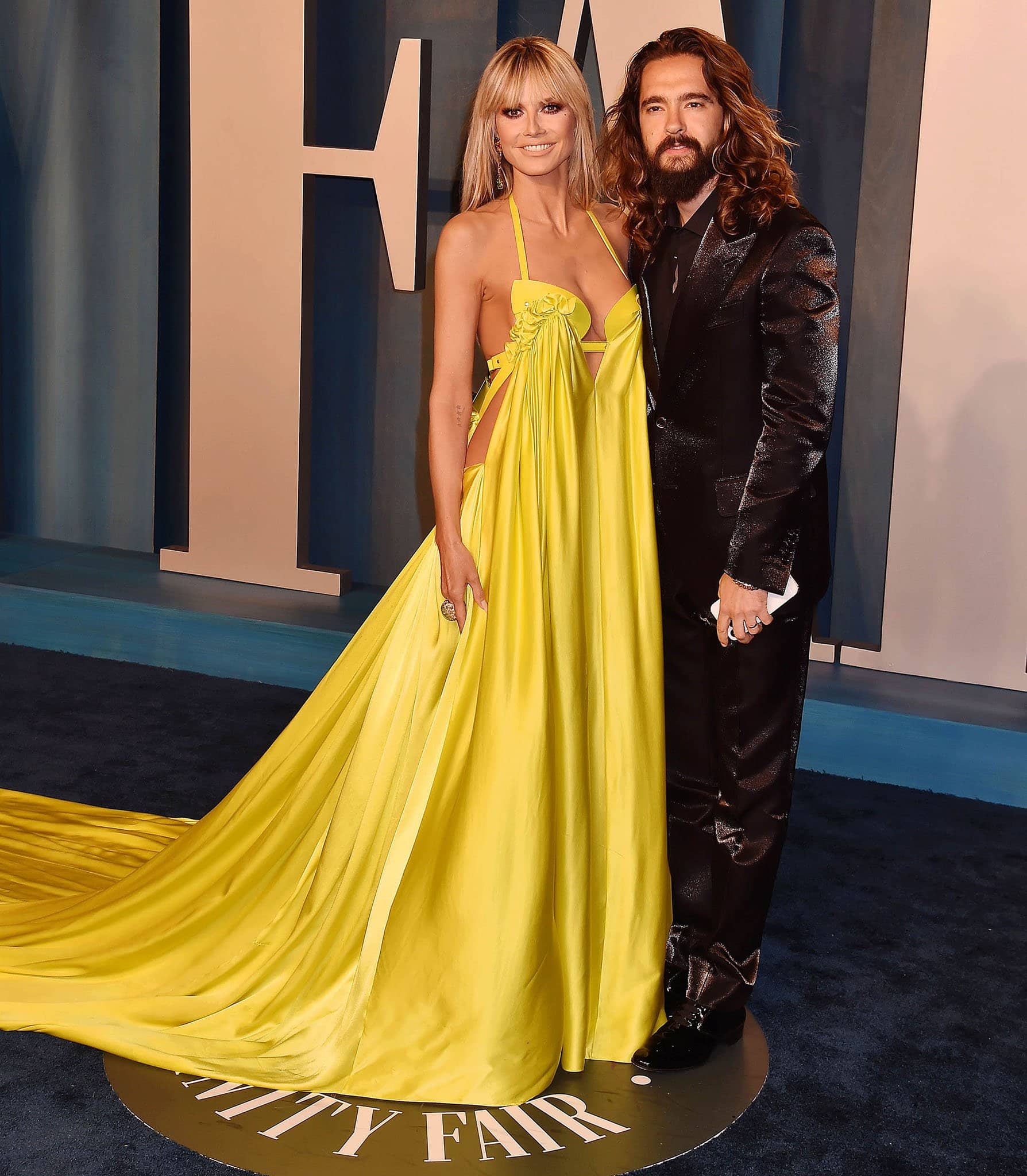 Heidi Klum poses with her husband Tom Kaulitz at the Vanity Fair Oscar Party in a yellow Az Factory gown with a structured bra and daring cutouts on March 27, 2022